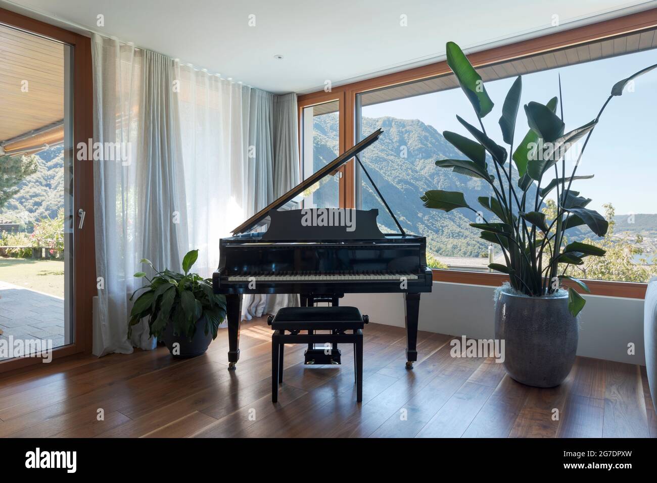 Schwarzes Klavier, Terrasse mit Garten. Großes Fenster mit Blick auf das Tal und den See. Niemand drinnen Stockfoto