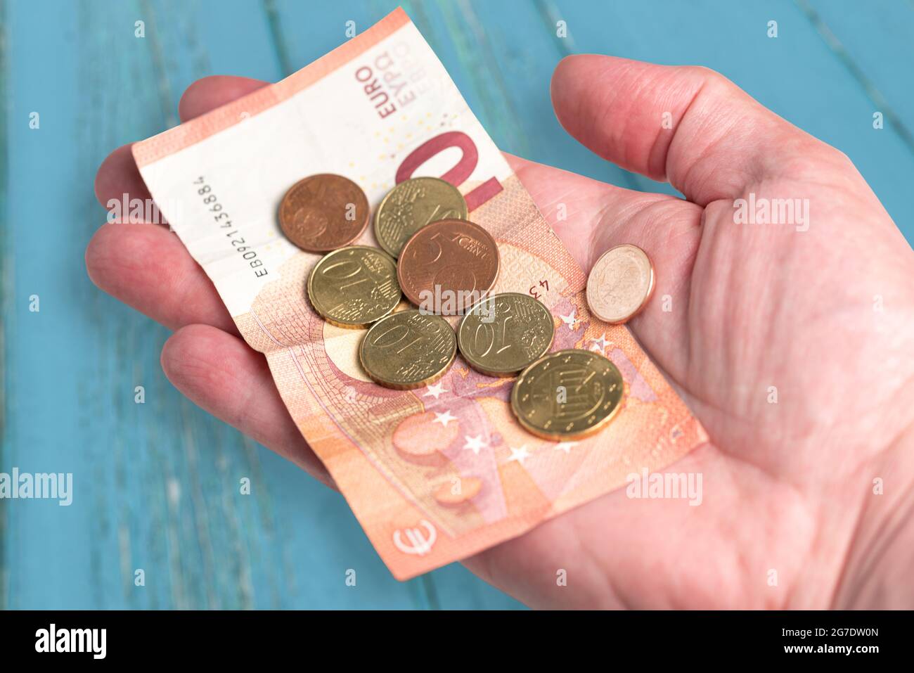 Hand mit 10 Euro Schein und kleinem Wechselgeld gegen blauen Holztisch Hintergrund Stockfoto