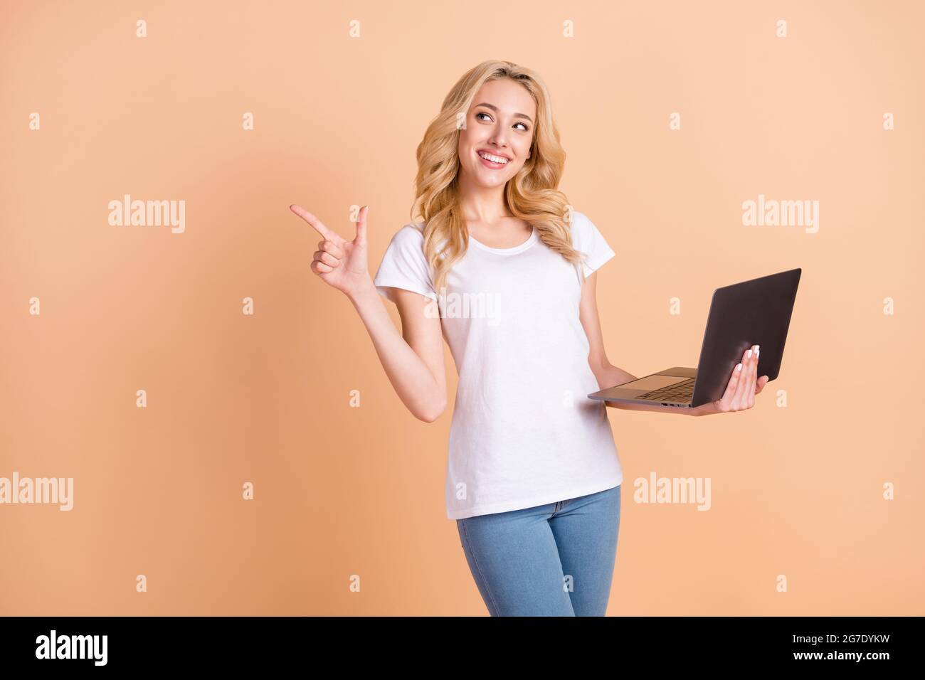Portrait Foto blonde Frau neugierig zeigen Copyspace halten Laptop isoliert pastellbeige Farbe Hintergrund Stockfoto
