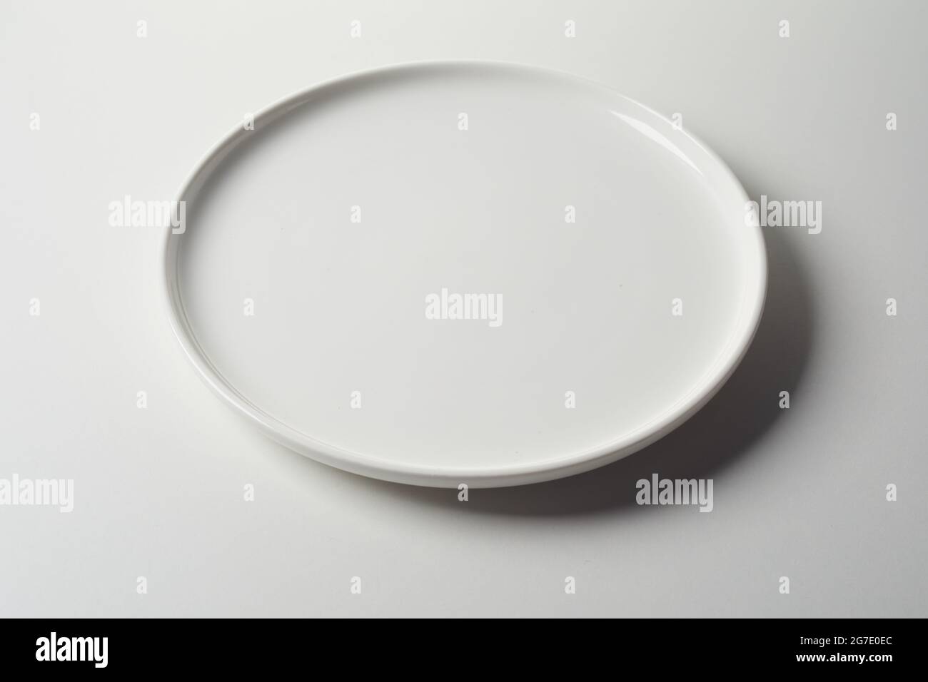 Catering-Konzept mit sauberer leerer weißer runder Keramikplatte mit erhobener Lippe auf weißem Studiohintergrund in einem hohen Winkel mit Schatten Stockfoto