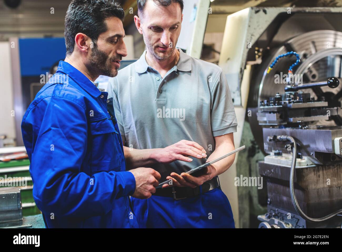 Zwei Arbeiter diskutieren ein Projekt vor der CNC-Drehmaschine schreiben in Zwischenablage Stockfoto