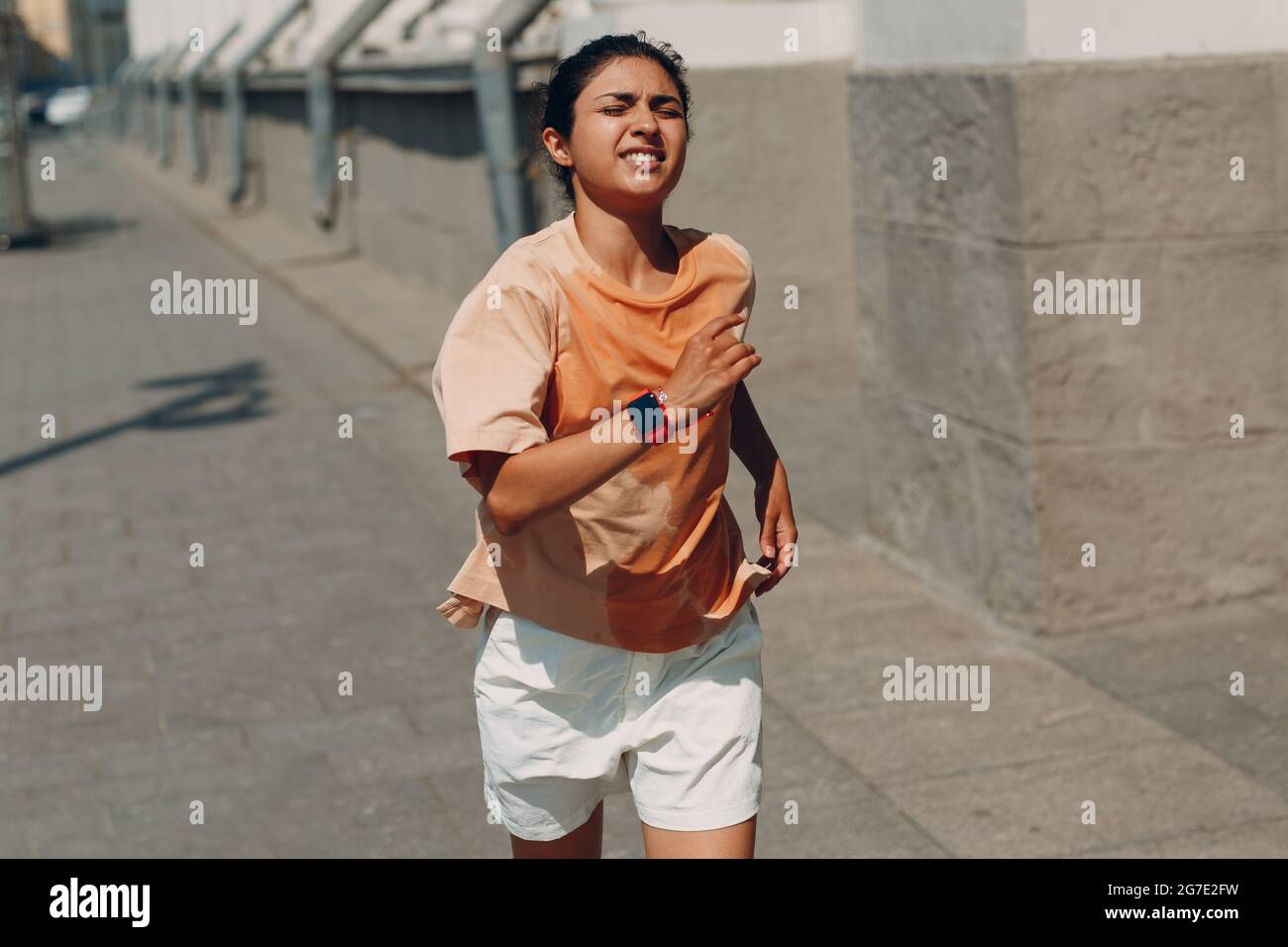 Junge indische Läuferin joggt in nassem, schweißtreibendem T-Shirt auf der City Street. Stockfoto
