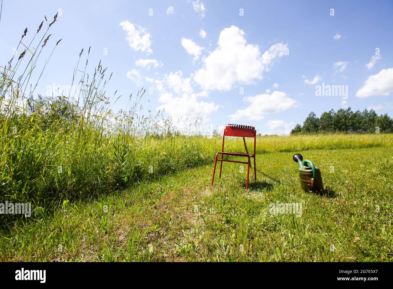 Roter Stuhl und Gießkanne auf der grünen Sommerwiese in der Natur. Stockfoto