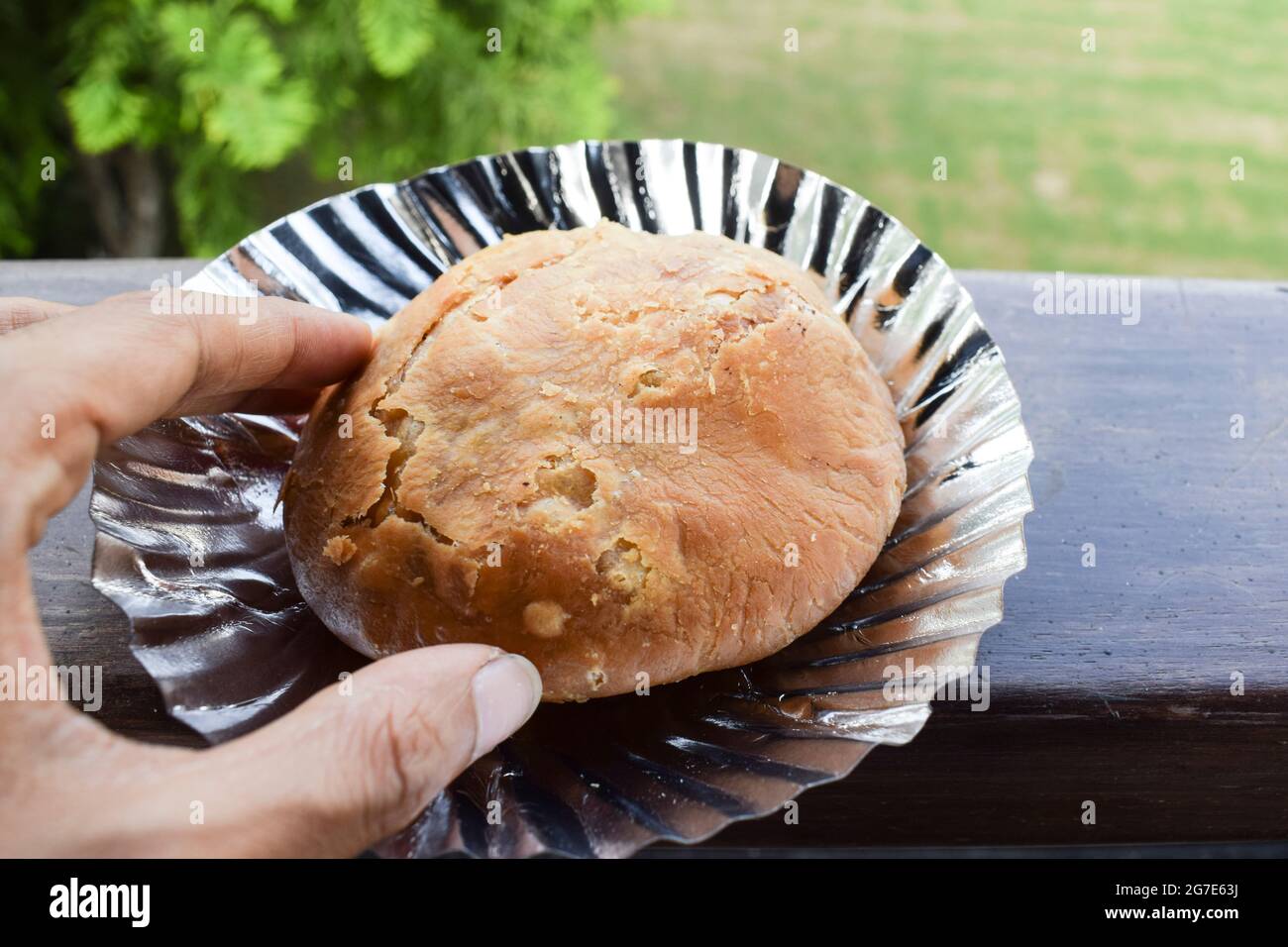 Weibliche essen Mung dal Kachori Snack-Artikel. Person Hand hält Kachouri. Im Freien Natur Hintergrund auf Tisch Balkon. Indische Frühstückssnacks Stockfoto