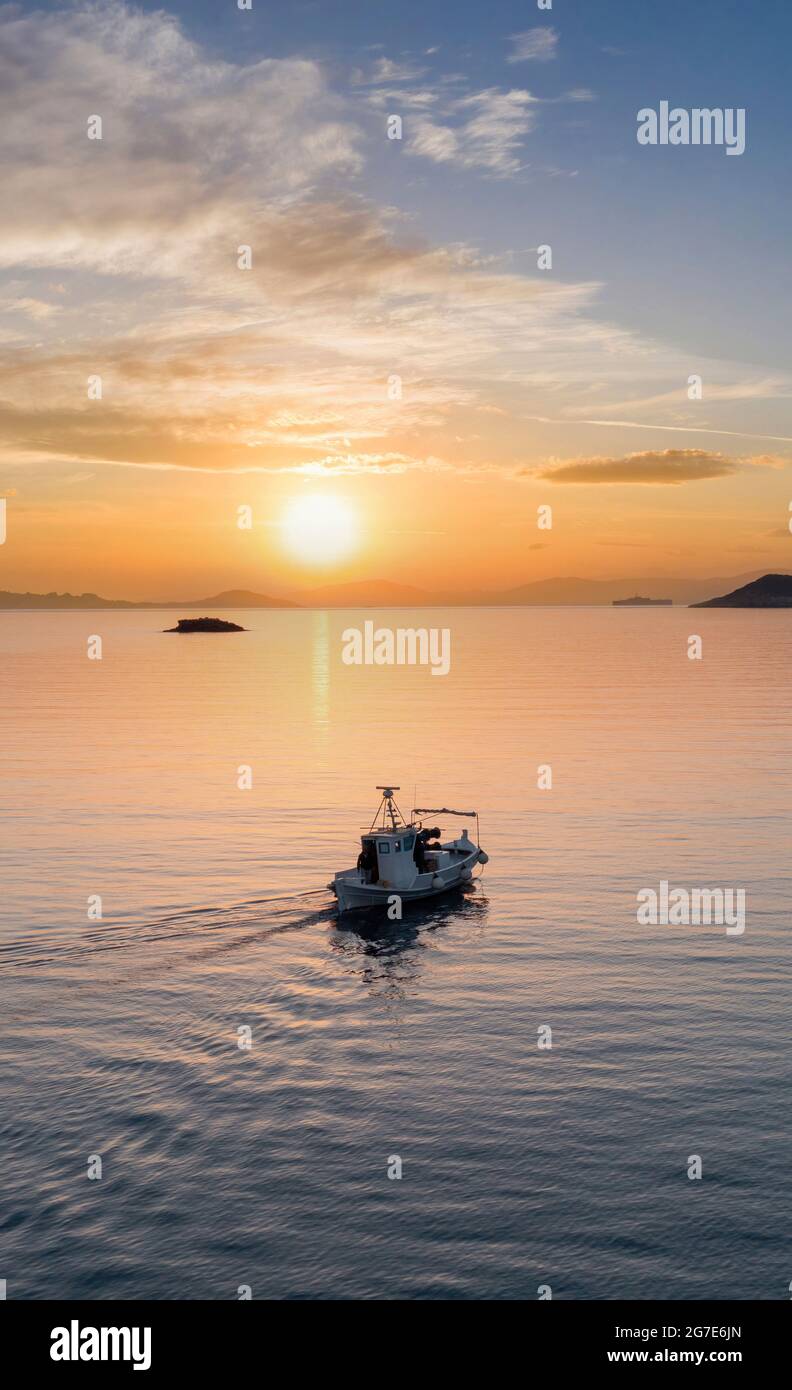 Fischerboot bei Sonnenuntergang. Kykladen-Insel. Griechenland. Luftdrohnenansicht eines typischen hölzernen Fischerbootes, das sich auf einem ruhigen Meer und einem orangefarbenen Himmel bewegt Stockfoto