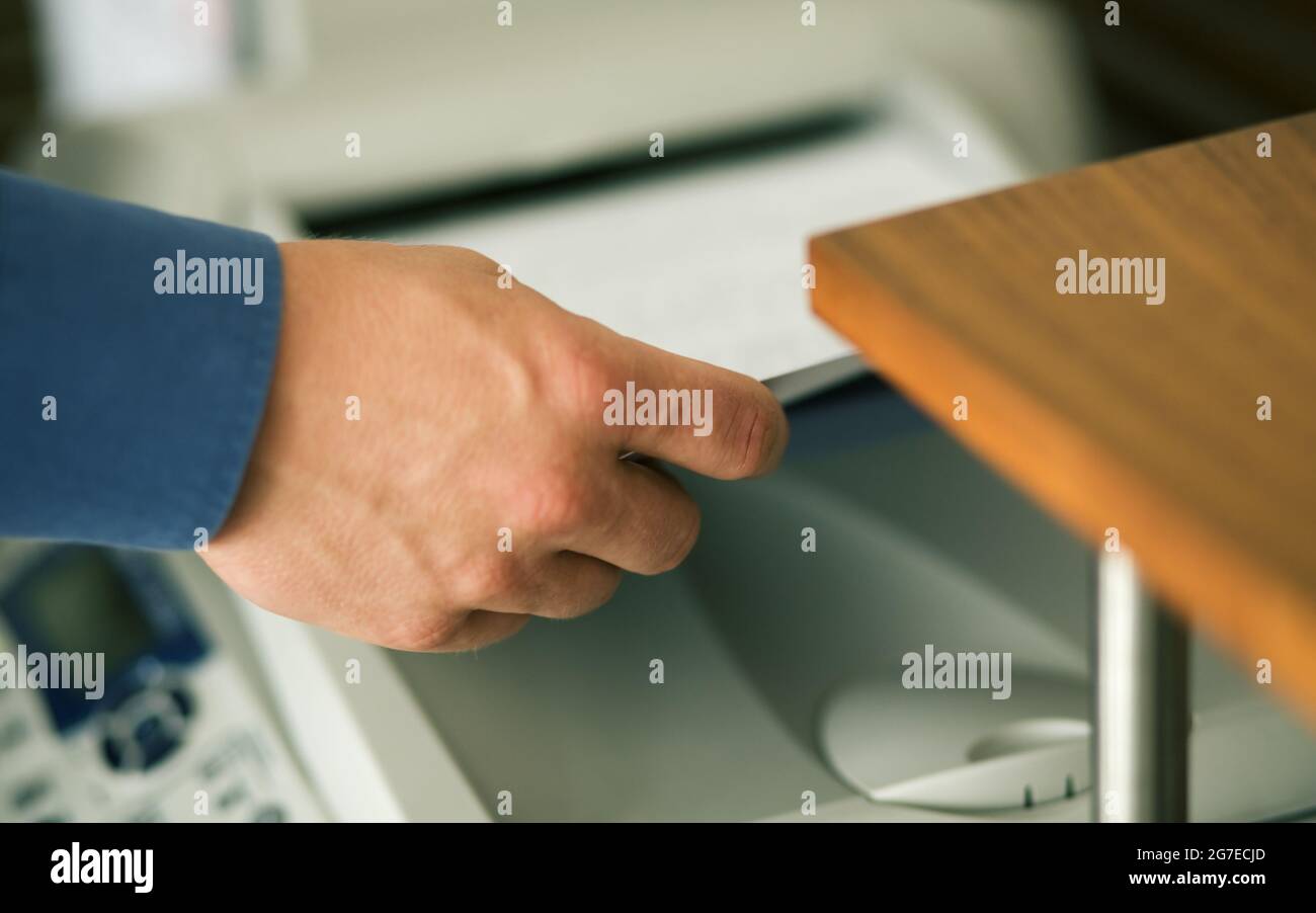 Ein Mann (nur eine Hand zu sehen) faxt einen Stapel Papier oder nimmt es aus einem Drucker Stockfoto