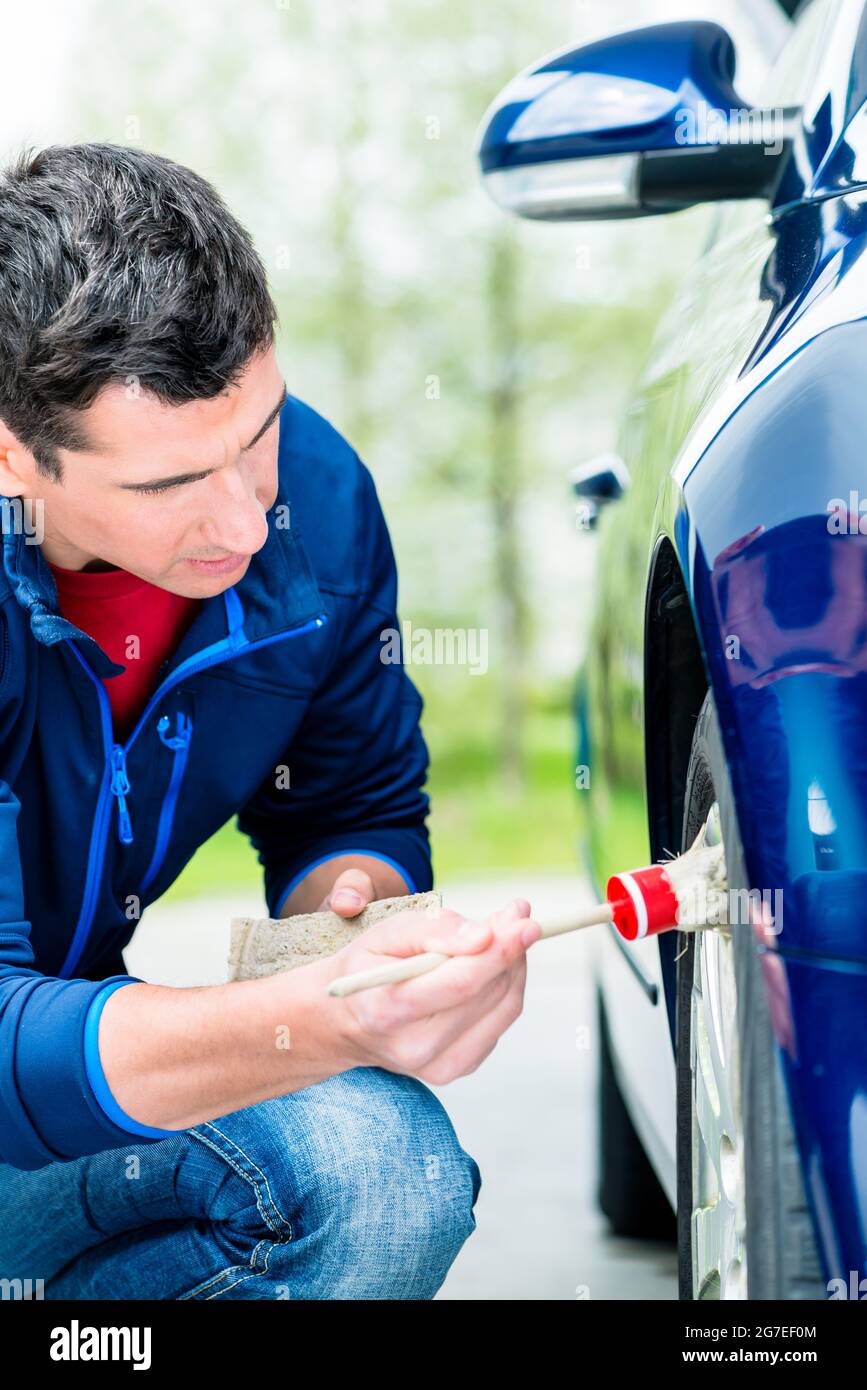Mann Reinigung der Leichtmetallfelgen Radnabe seines Autos klagt, einer weichen Bürste und der Seife zwischen den Speichen zu erhalten Stockfoto