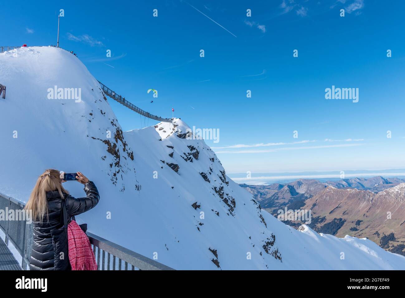 Unbekannte Frau, die mit ihrem Mobiltelefon Fotos von einer Person macht, die im Berg Gleitschirmfliegen macht. Stockfoto