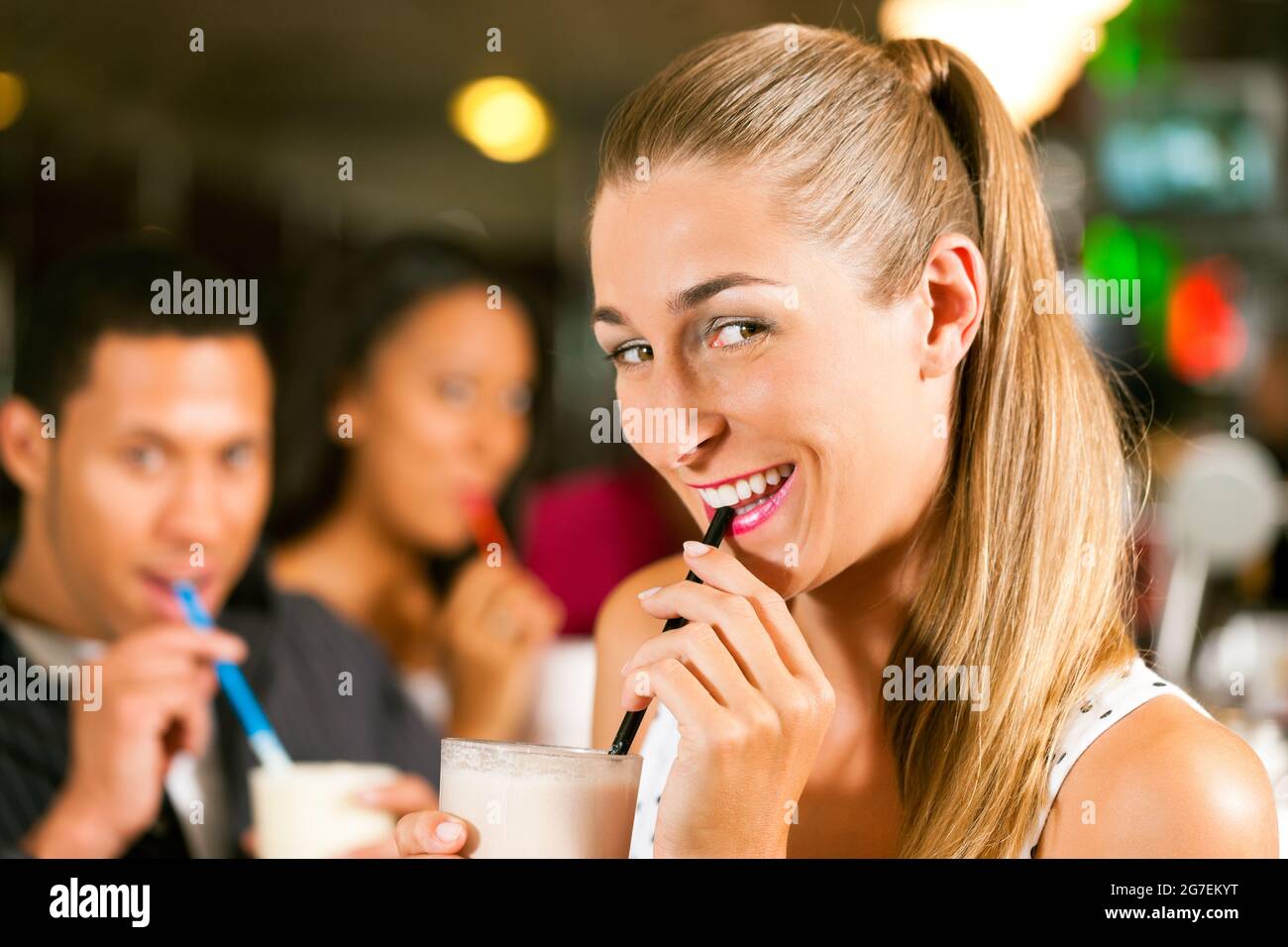 Freunde trinken Milchshakes in einer Bar und haben viel Spaß; konzentrieren Sie sich auf die Frau davor Stockfoto