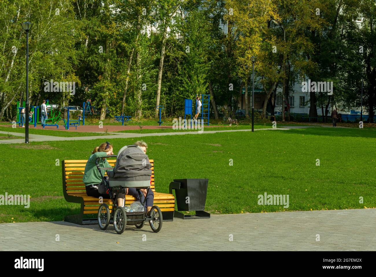 Zwei Frauen sprechen auf einer Parkbank, während sie ein neugeborenes Baby in einem Kinderwagen schaukeln. Stockfoto