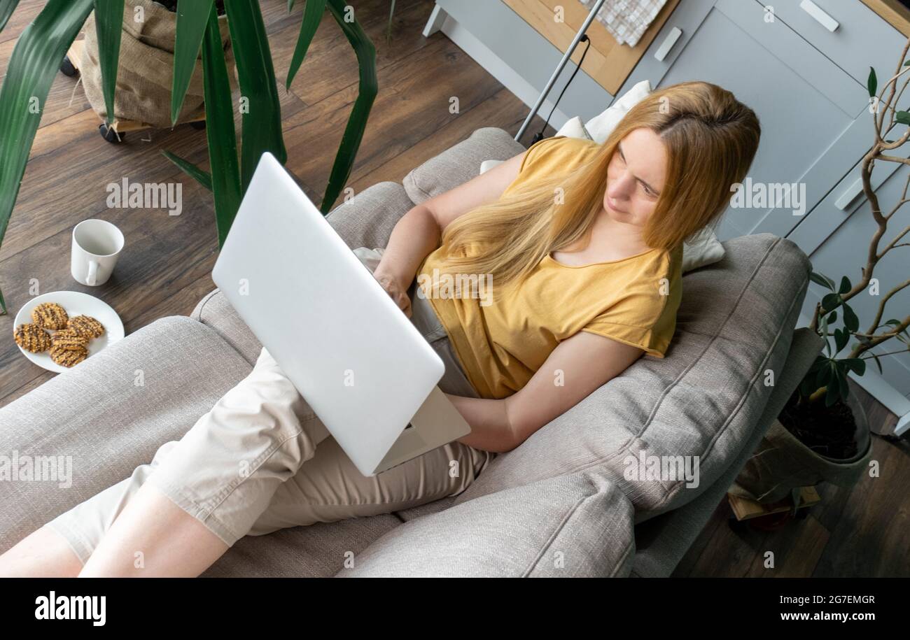 Blonde Frau mittleren Alters sitzt auf dem Sofa und kommuniziert online per Laptop. Stockfoto