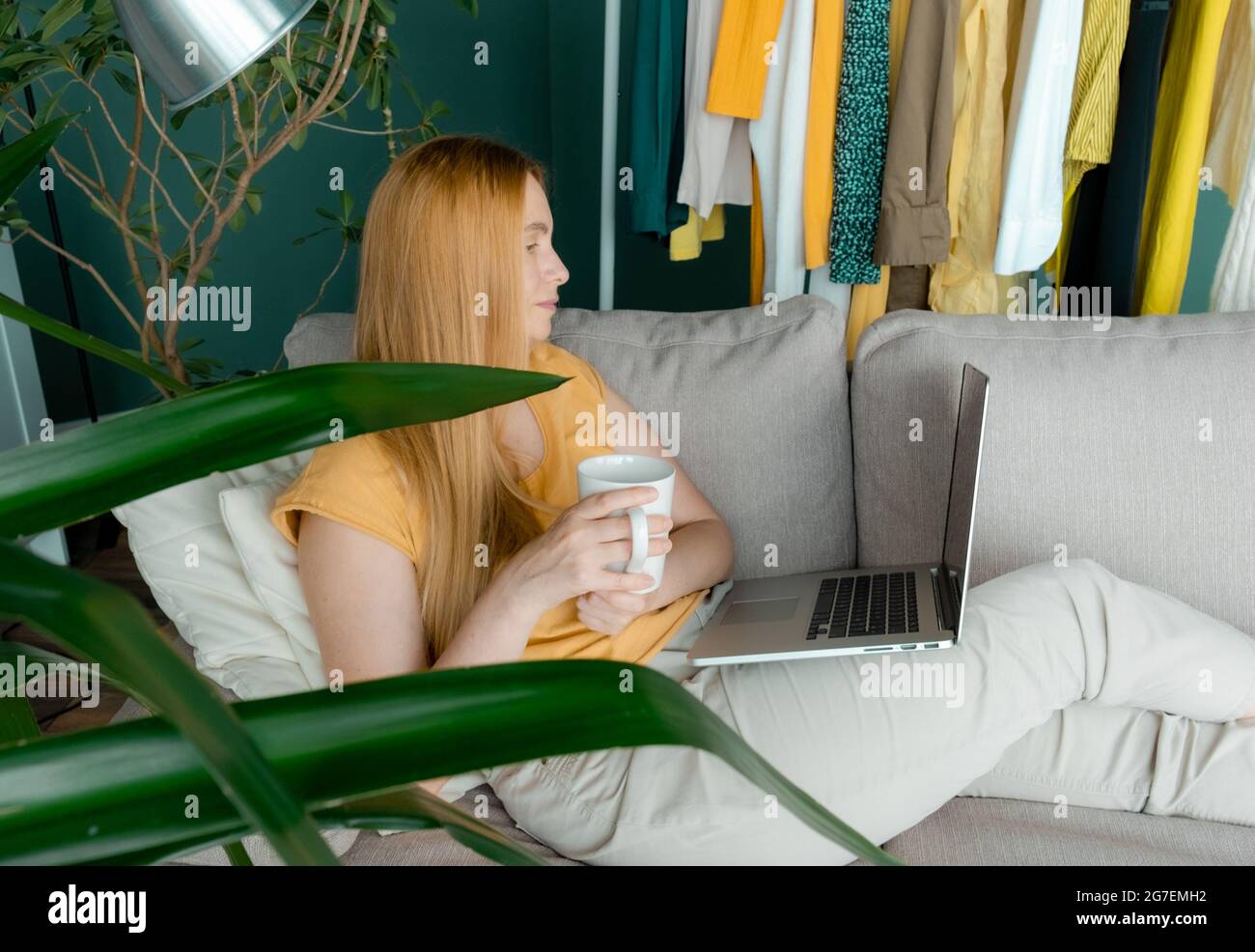 Blonde Frau mittleren Alters sitzt auf dem Sofa und kommuniziert online per Laptop. Stockfoto