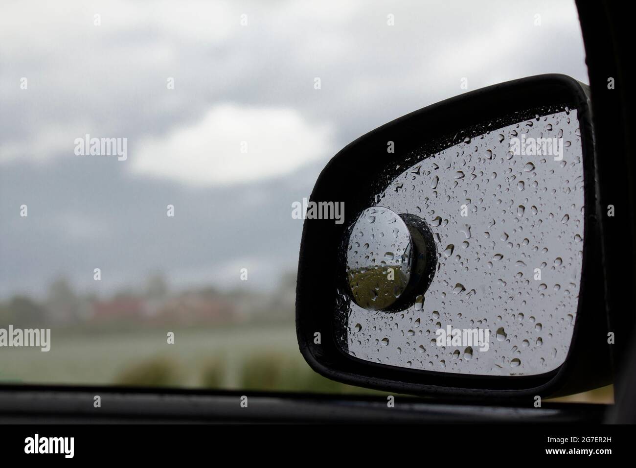 Regentropfen auf einem Autospiegel vor dem Hintergrund von Regenwolken. Stockfoto
