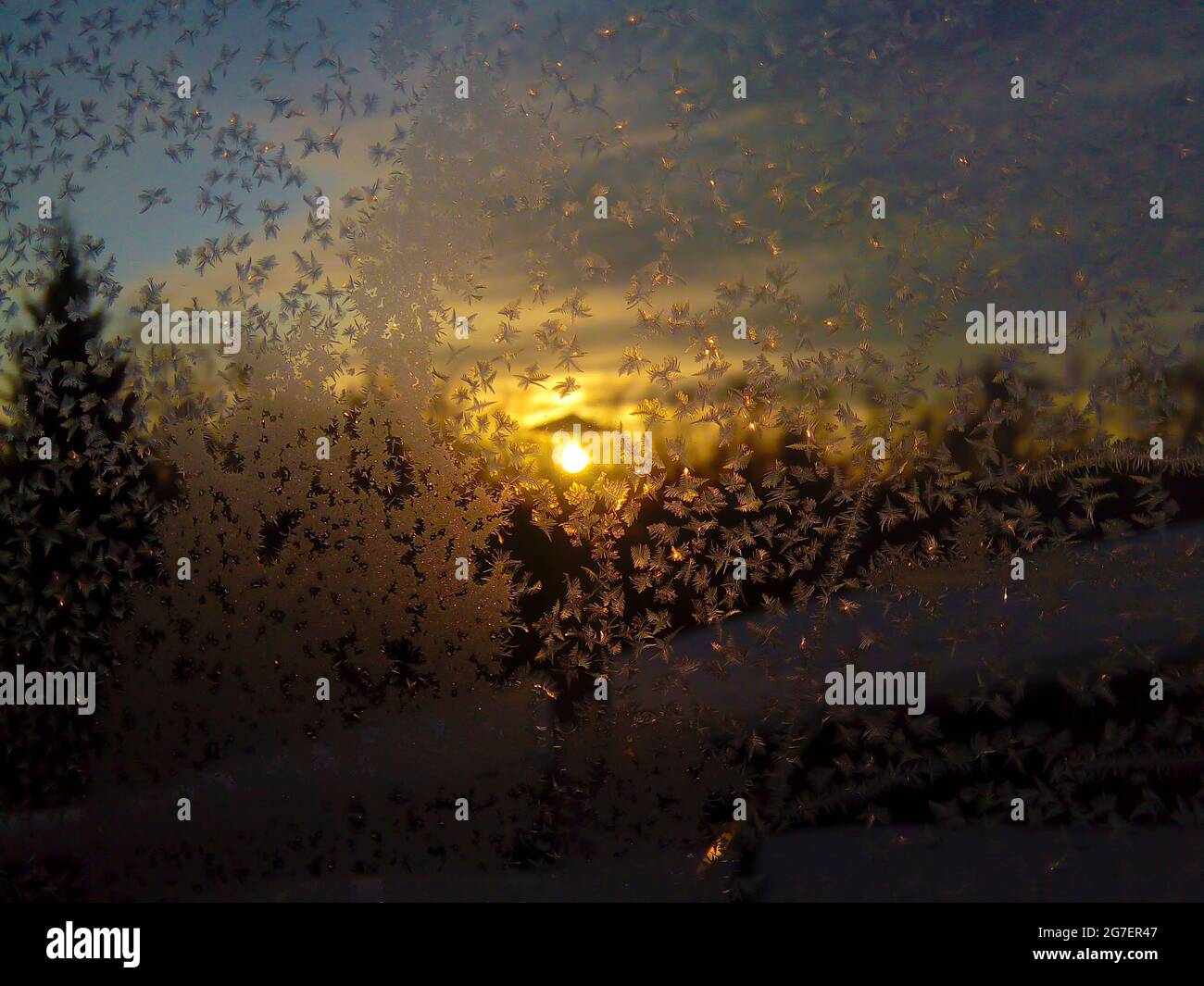 Eismuster auf einem Winterfenster auf einem Sonnenuntergangshintergrund. Bizarre Formen des Rauhfrosts auf einem gefrorenen Winterfenster. Stockfoto