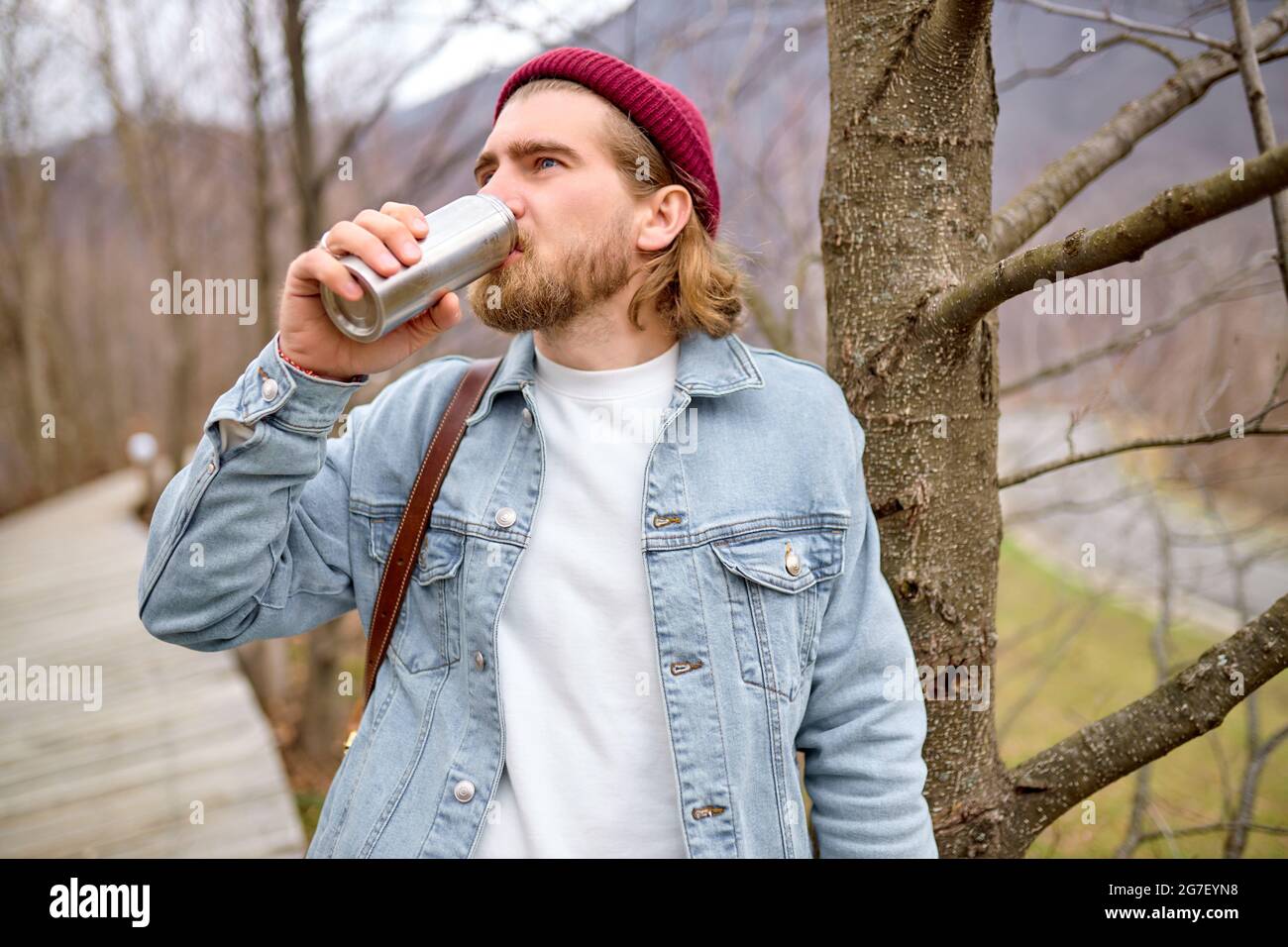 Junger, hübscher, brutaler bärtiger Mann, der in der wilden Natur mit Thermoskannen, im Herbst- oder Frühlingsstil reist, hat sich als Reisender in legerer Kleidung ausruhen können und steht als nächstes Stockfoto
