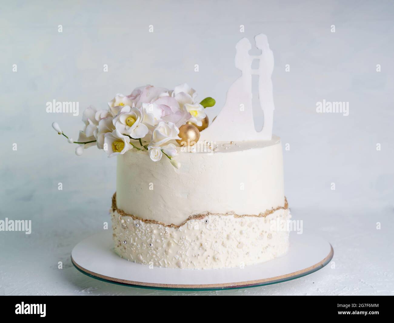 Beige Hochzeitstorte mit Blumen und Figuren von Braut und Bräutigam auf der Oberseite. Einstufiger Hochzeitstorte auf weißem Hintergrund Stockfoto