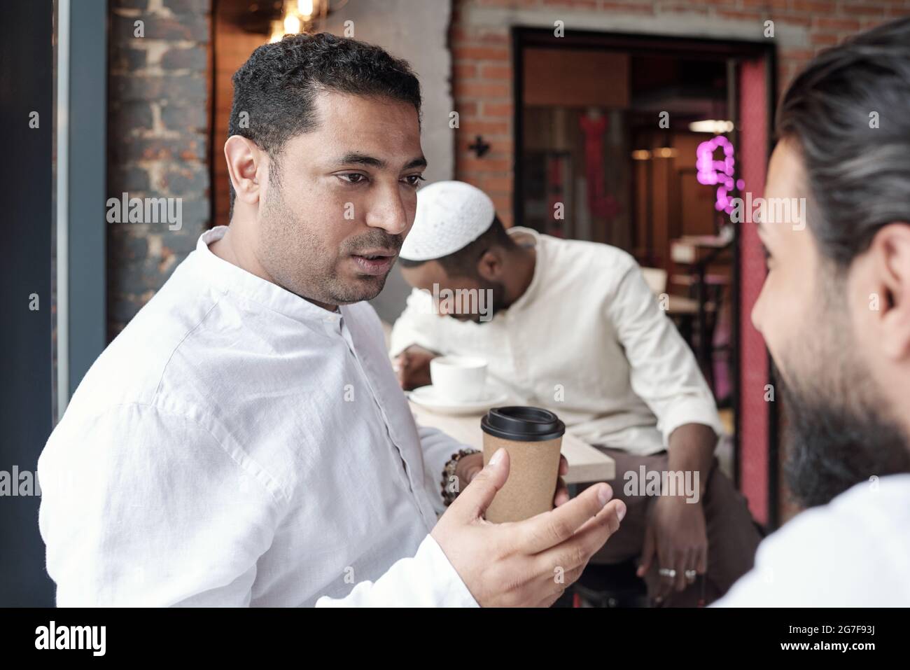 Ein arabischer Mann mittleren Alters stachelte Hand, während er mit einem Freund sprach und Kaffee im Café trank Stockfoto