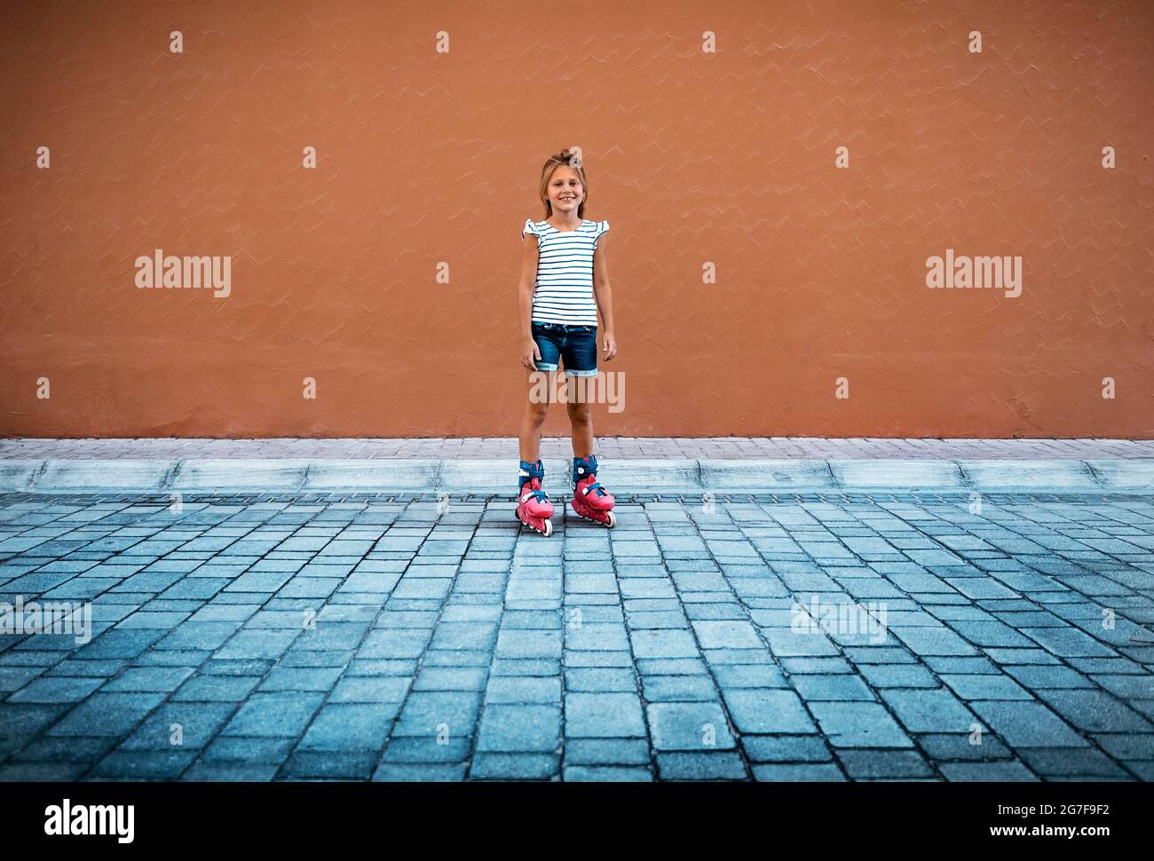 Nette glückliche kleine Mädchen Rollerblading im Hof. Viel Spaß Im Freien. Perfekte Sommerrekreation. Gesundes Sportliches Sommerurlaube-Konzept. Stockfoto