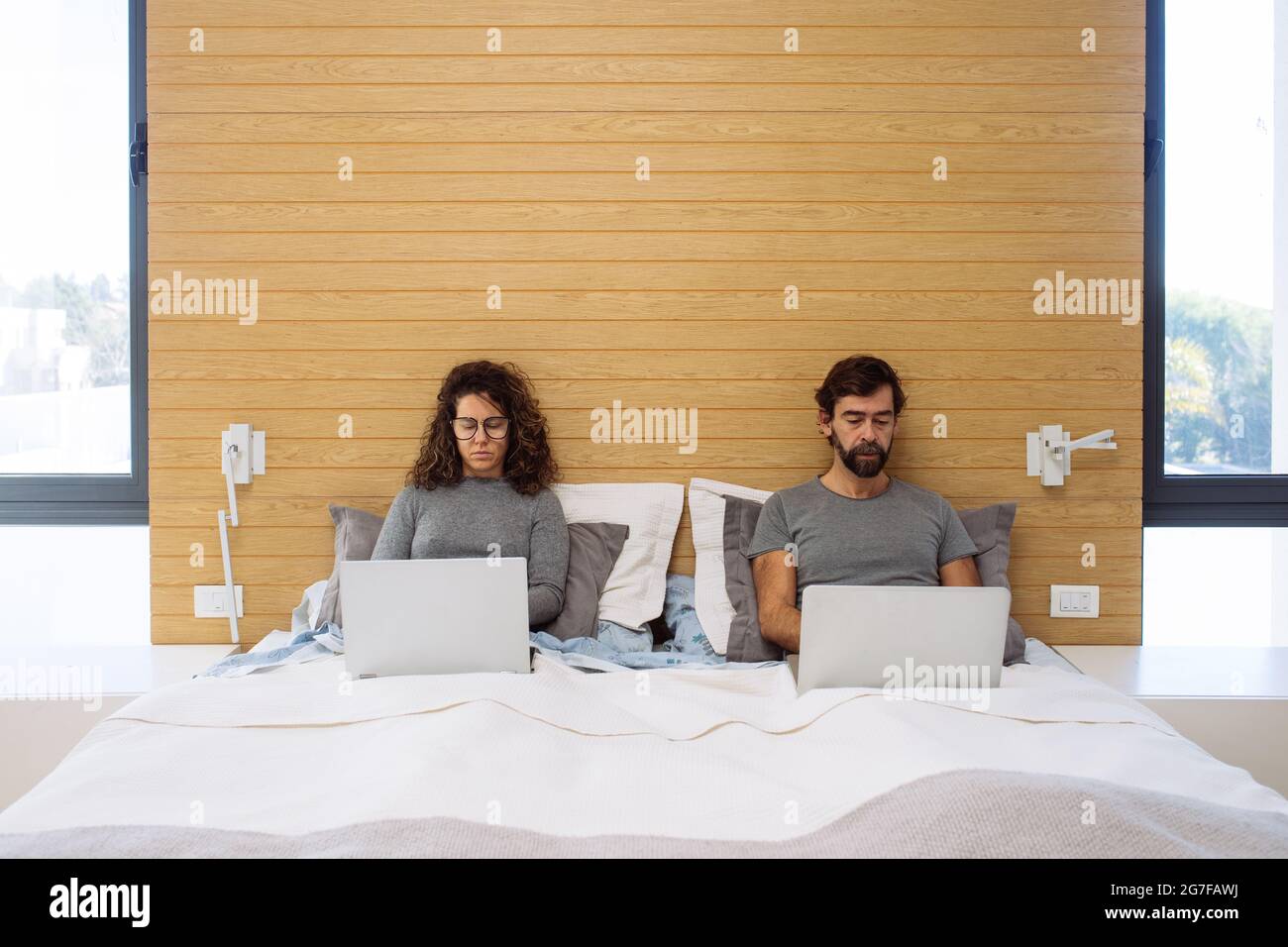 Paar in einem Doppelbett King Size mit jeweils ihrem Notebook arbeiten konzentriert beobachten jeden ihrer Bildschirme. Konzept: Home Office arbeitet vom Bett aus Stockfoto