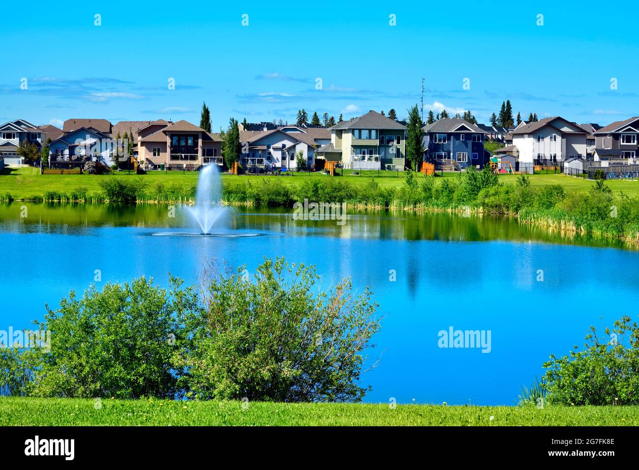 Eine urbane Landschaft mit Grünflächen, Teich, Häusern und blauem Himmel in Morinville Alberta, Kanada. Stockfoto