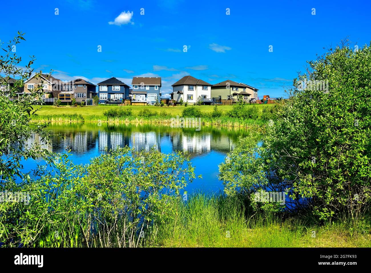 Eine urbane Landschaft mit Grünflächen, einem Teich, Häusern und blauem Himmel in Morinville, Alberta, Kanada. Stockfoto