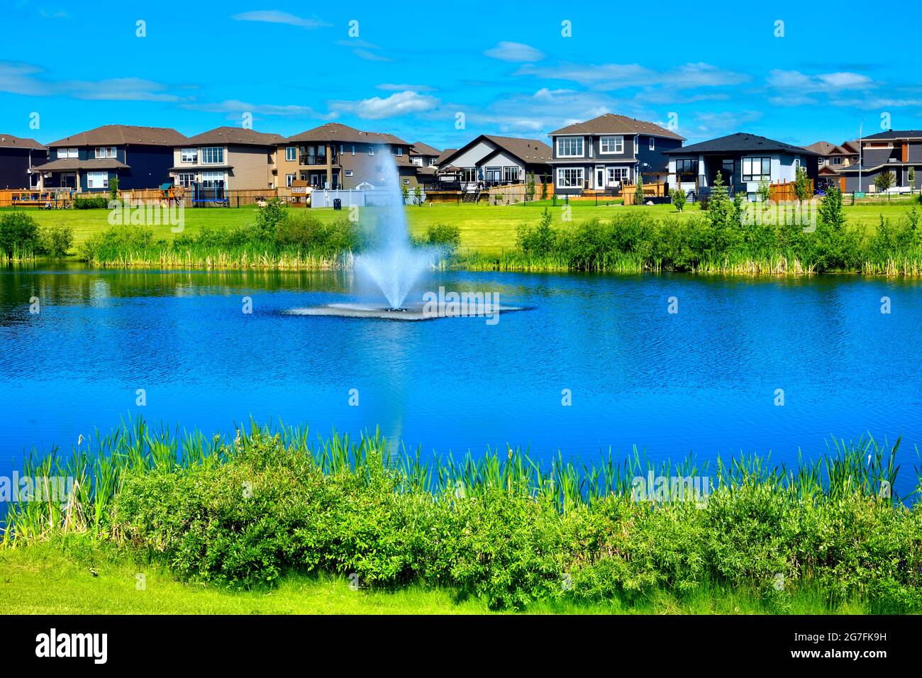 Urbanes Leben mit Grünflächen, einem Teich, Häusern und blauem Himmel in Morinville, Alberta, Kanada. Stockfoto