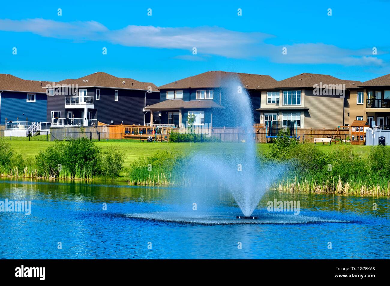 Urbanes Leben mit Grünflächen, einem Teich, Häusern und blauem Himmel in Morinville, Alberta, Kanada. Stockfoto
