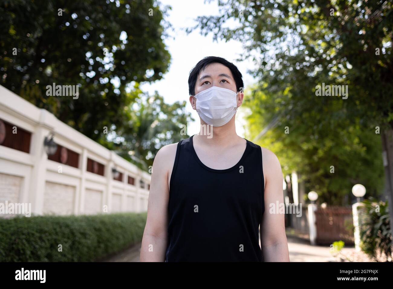 Junger asiatischer Mann, der mit einer Gesichtsmaske in der Stadt läuft. Laufmännchen trainieren und joggen auf der Straße Stockfoto