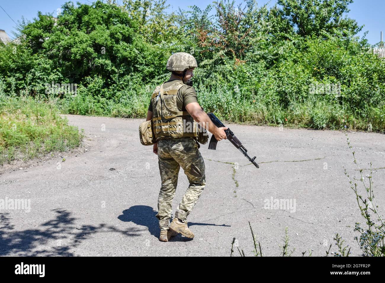 Ukrainischer Soldat, der an einer verlassenen Straße im Vorort Marinka vorbei geht. Marinka, eine kleine Stadt in der Ostukraine, liegt an der Front des Konflikts. Nach einem umfassenden Waffenstillstand in der zweiten Jahreshälfte 2020 haben die Spannungen in der Ostukraine im Jahr 2021 zugenommen. Die Ukraine verfügt mit rund 200,000 aktiven Soldaten über die drittgrößte Armee Europas. Stockfoto