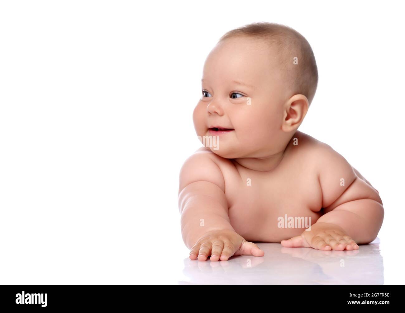 Lächelnd, kichernd Kleinkind Baby Mädchen Kind in Windel liegt auf ihrem Bauch mit ausgestrecktem Arm und schaut zur Seite Stockfoto