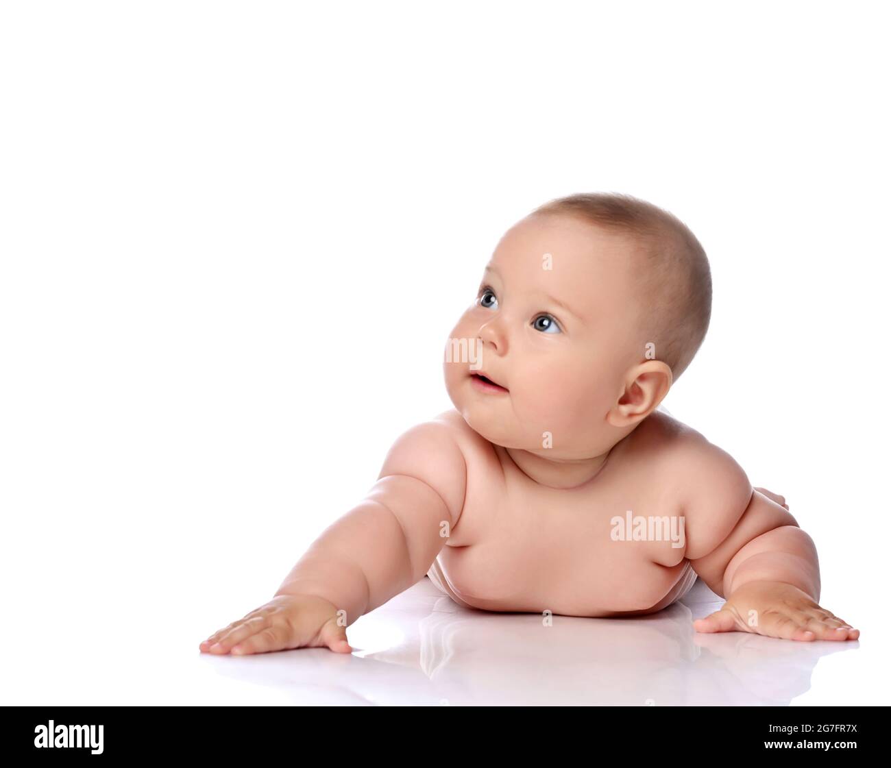 Neugierig Kleinkind Baby Mädchen Kind in Windel liegt auf ihrem Bauch mit ausgestrecktem Arm und Blick auf die obere Ecke Stockfoto