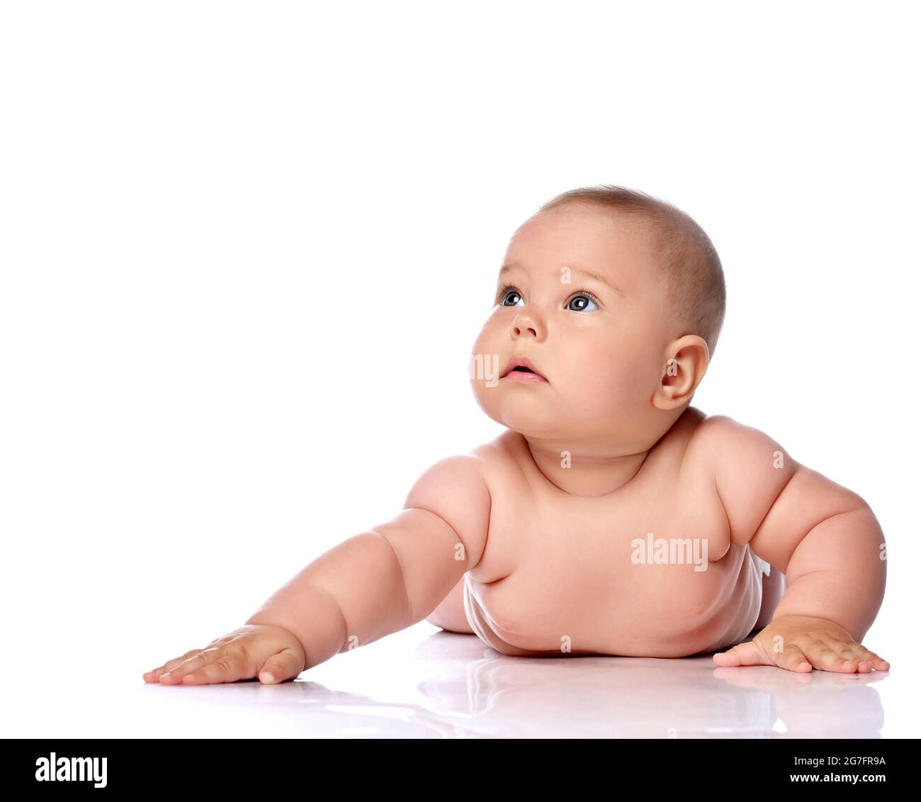 Ruhig und konzentriert Kleinkind Baby Mädchen Kind in Windel liegt auf ihrem Bauch mit ausgestrecktem Arm und Blick nach oben Stockfoto