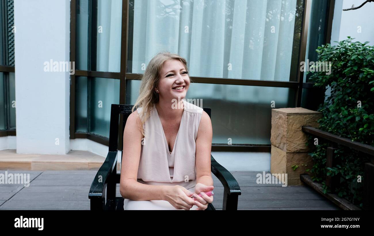 Osteuropäische kaukasische Frau mittleren Alters blondes Haar helle Haut blassen Teint tragen cremefarbenen Sommerkleid Lässige Kleidung posiert sitzen Stockfoto