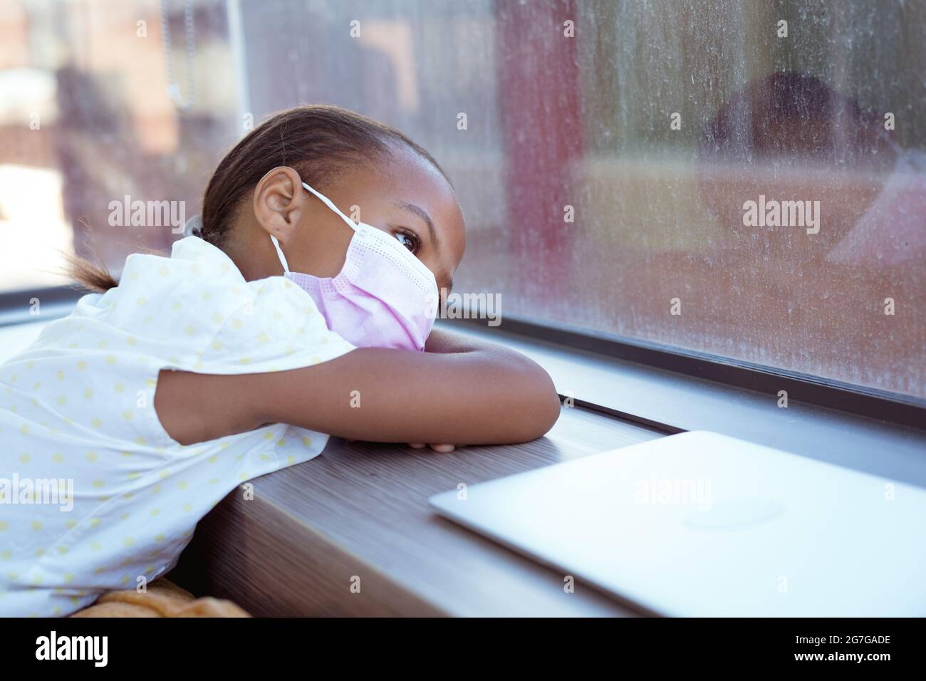 afroamerikanisches Schulmädchen mit Gesichtsmaske sitzt in der Schule Klassenzimmer Blick aus dem Fenster Stockfoto