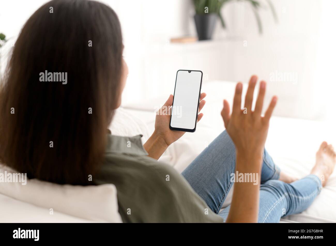 Indische Frau hält und nutzt Smartphone mit schwarzem leeren Bildschirm für die Videoverbindung, winkt Hallo in die Webcam, mit der neuen mobilen App für virtuelle Meetings. Mockup, Kopierfläche für Werbung Stockfoto