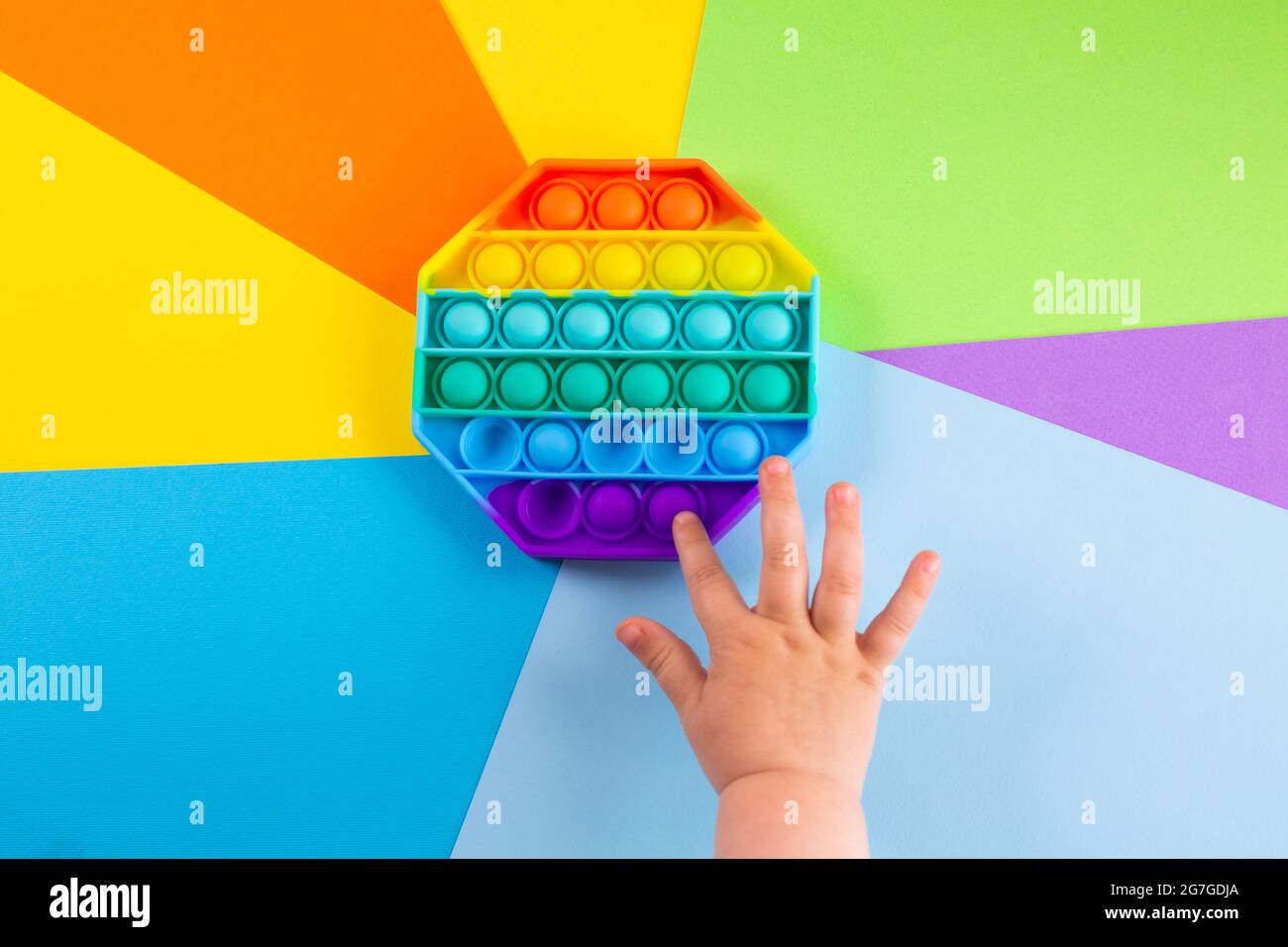 Kinder Hände schieben sensorische popit auf bunten Hintergrund. Antistress-Pop-it-Spielzeug. Rainbow Silikon sensorische Fidget Neue beliebte trendige Silikon-Spielzeug. Stockfoto