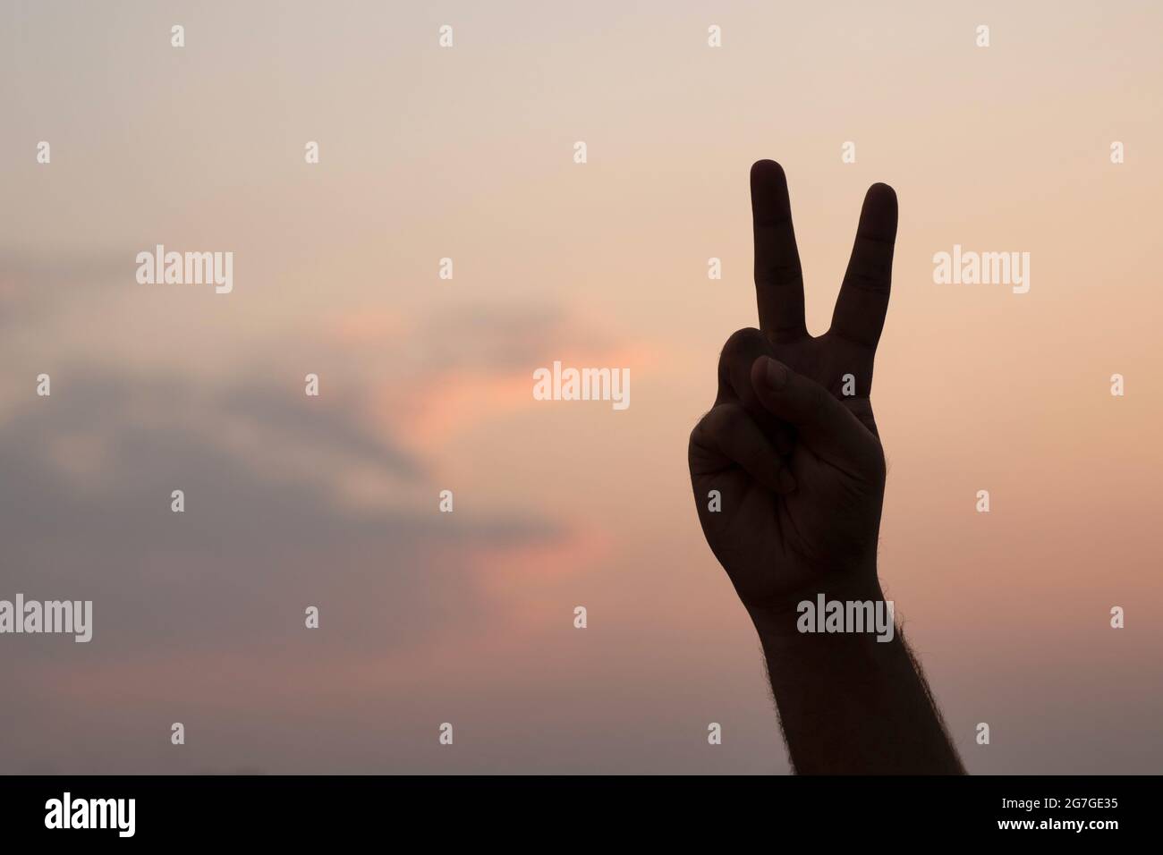 Mann, der das Friedenssymbol mit der Hand gegen den Abendhimmel kreist - Silhouette Stockfoto