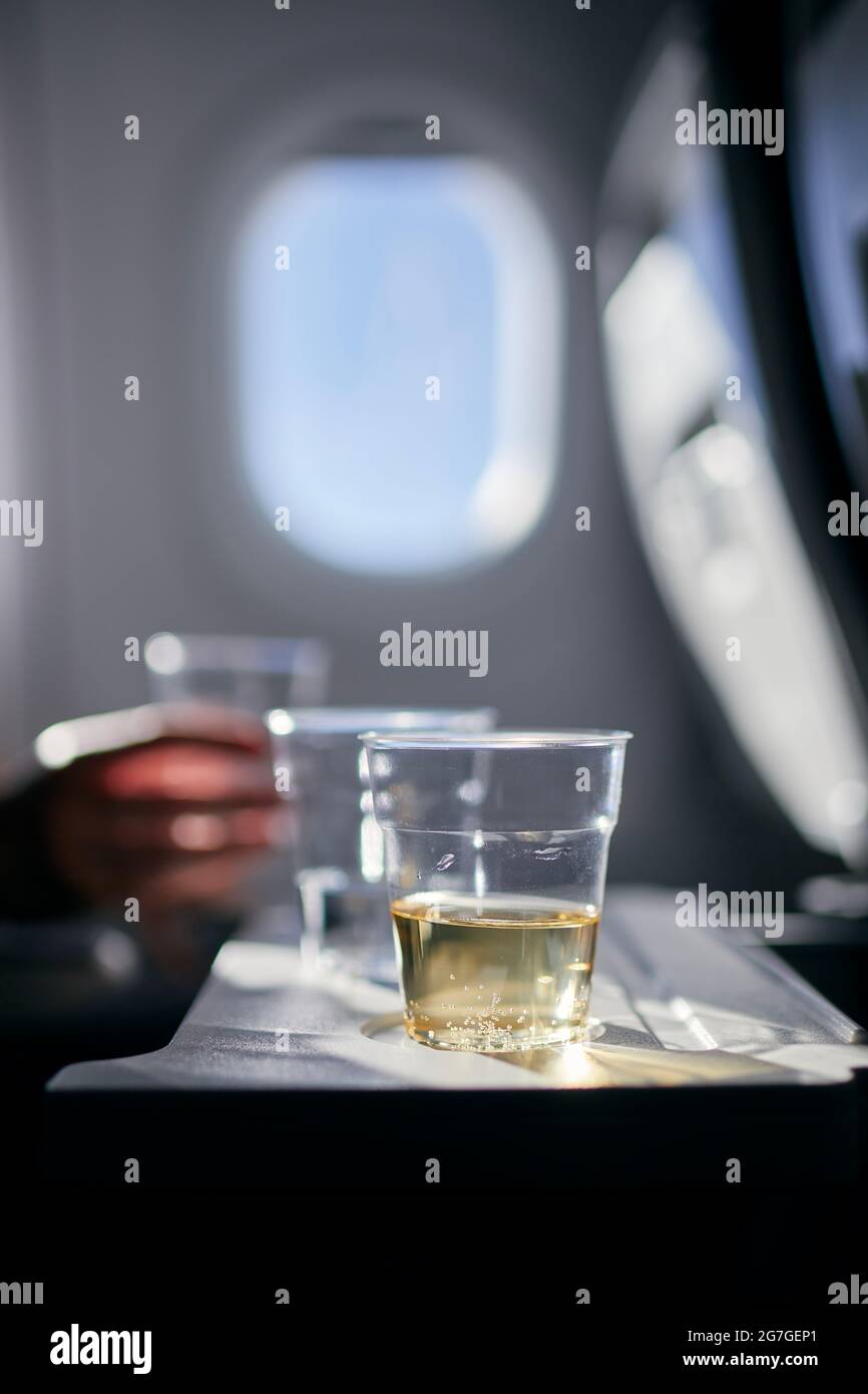 Einwegbecher mit Getränken (Wasser und Wein) auf dem Tisch vor dem Flugzeugfenster. Erfrischung während des Fluges. Stockfoto