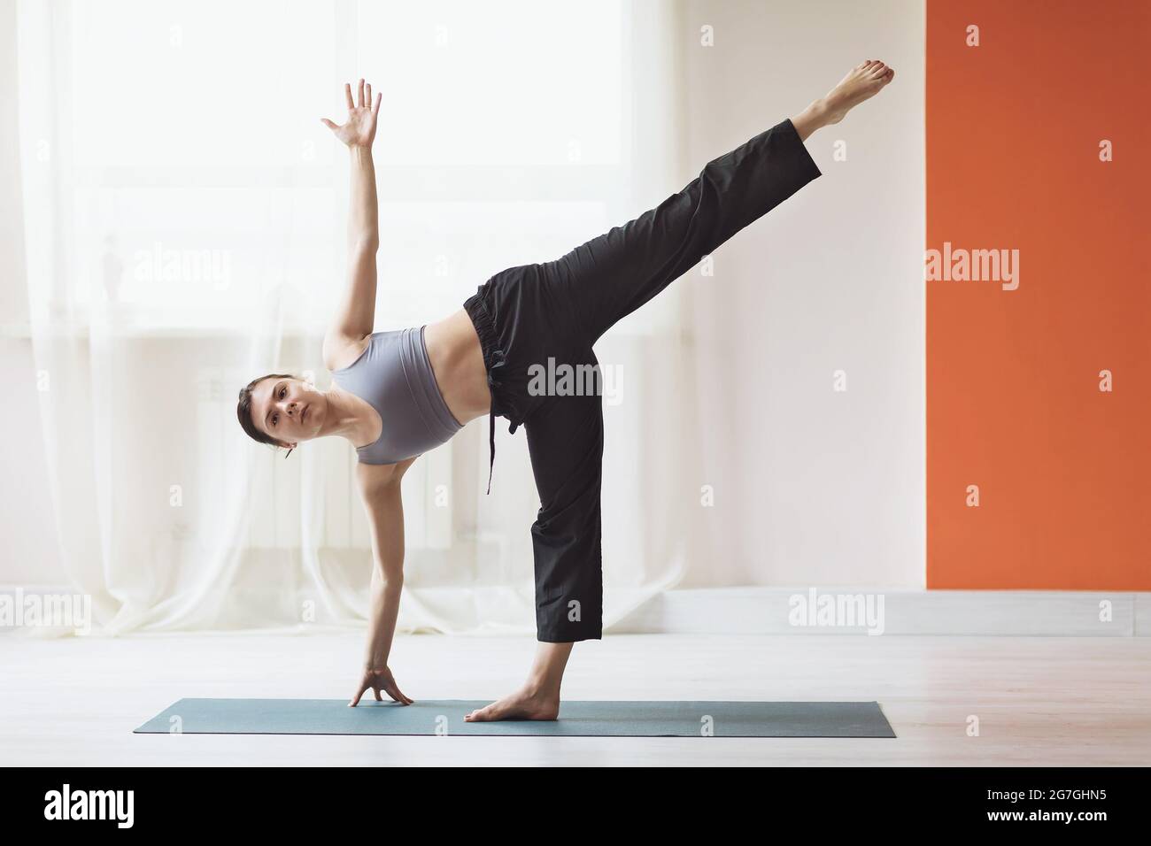 Junge Frau, die Yoga praktiziert, führt die Ardha Chandrasana-Übung durch, die Halbmondpose im Studio in der Nähe des Fensters Stockfoto