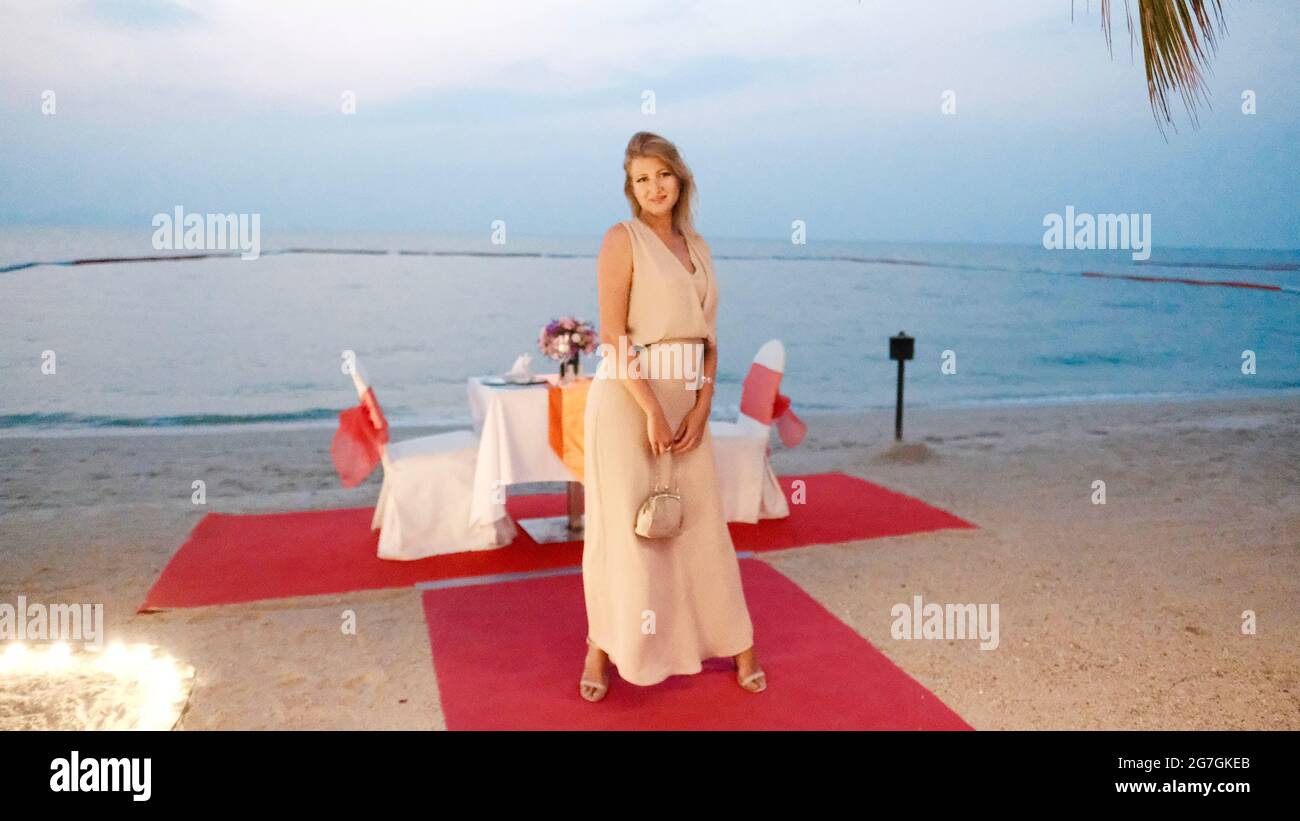 Osteuropäische kaukasische Frau mittleren Alters blondes Haar helle Haut blasse Teint in formeller Kleidung in der Nacht posiert auf dem roten Teppich und Sand Stockfoto