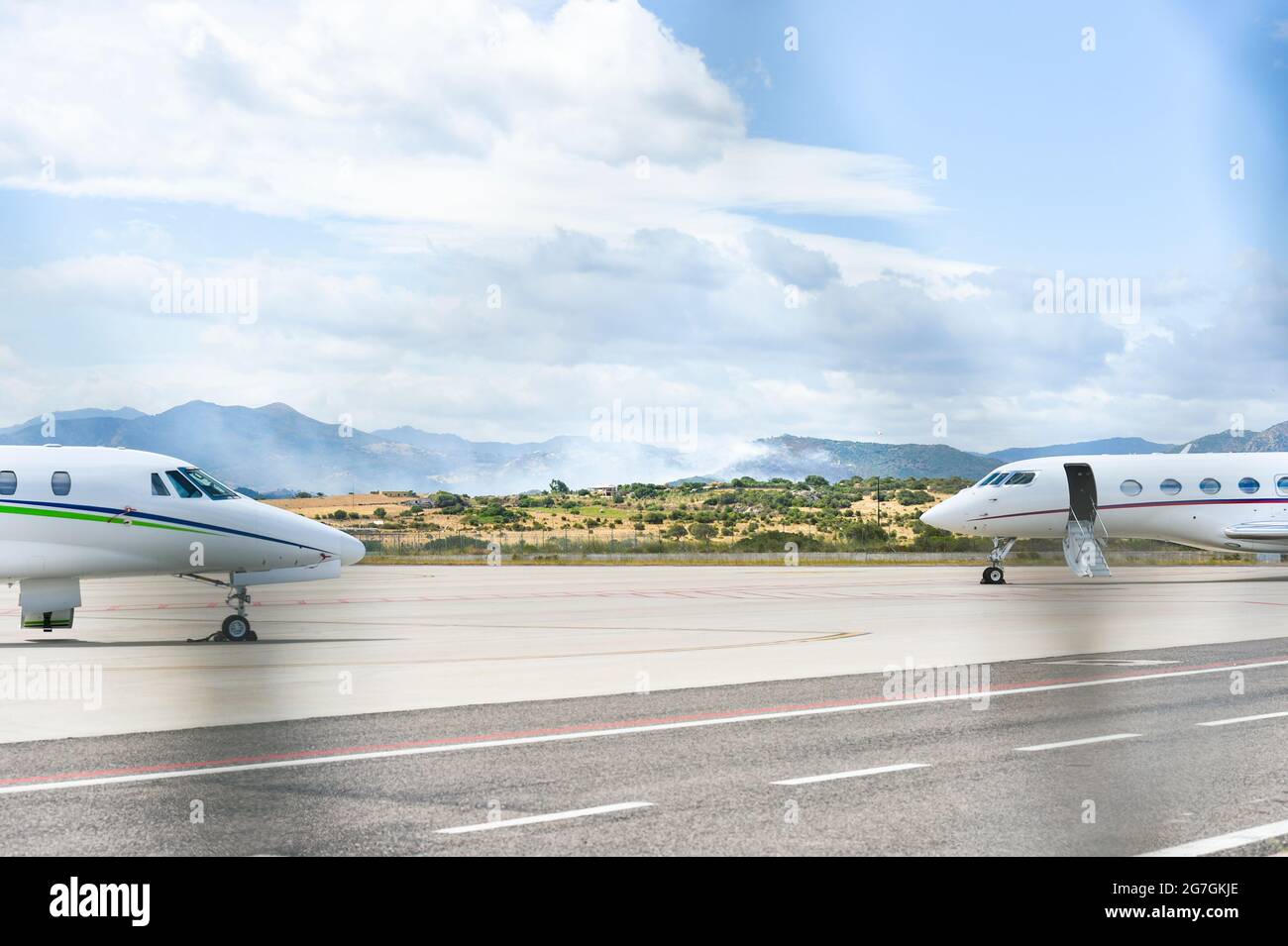 Blick auf ein Feuer in der Nähe des Flughafens Olbia Costa Smeralda mit Flugzeugen, die auf der Start- und Landebahn abgestellt sind Stockfoto