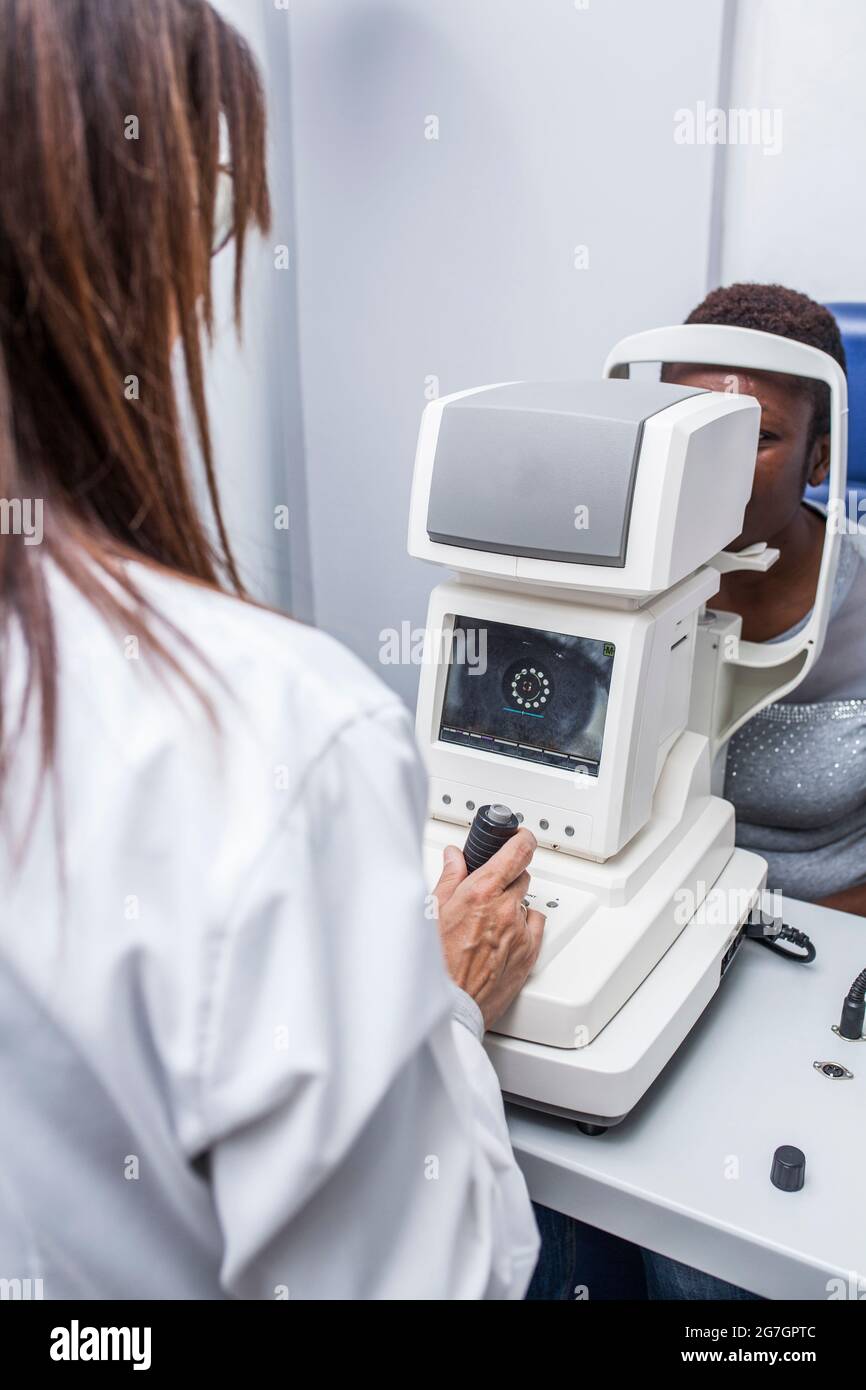 Optiker, der den Retinograph während der Untersuchung des Sehvermögens einer schwarzen Frau anpasst Stockfoto