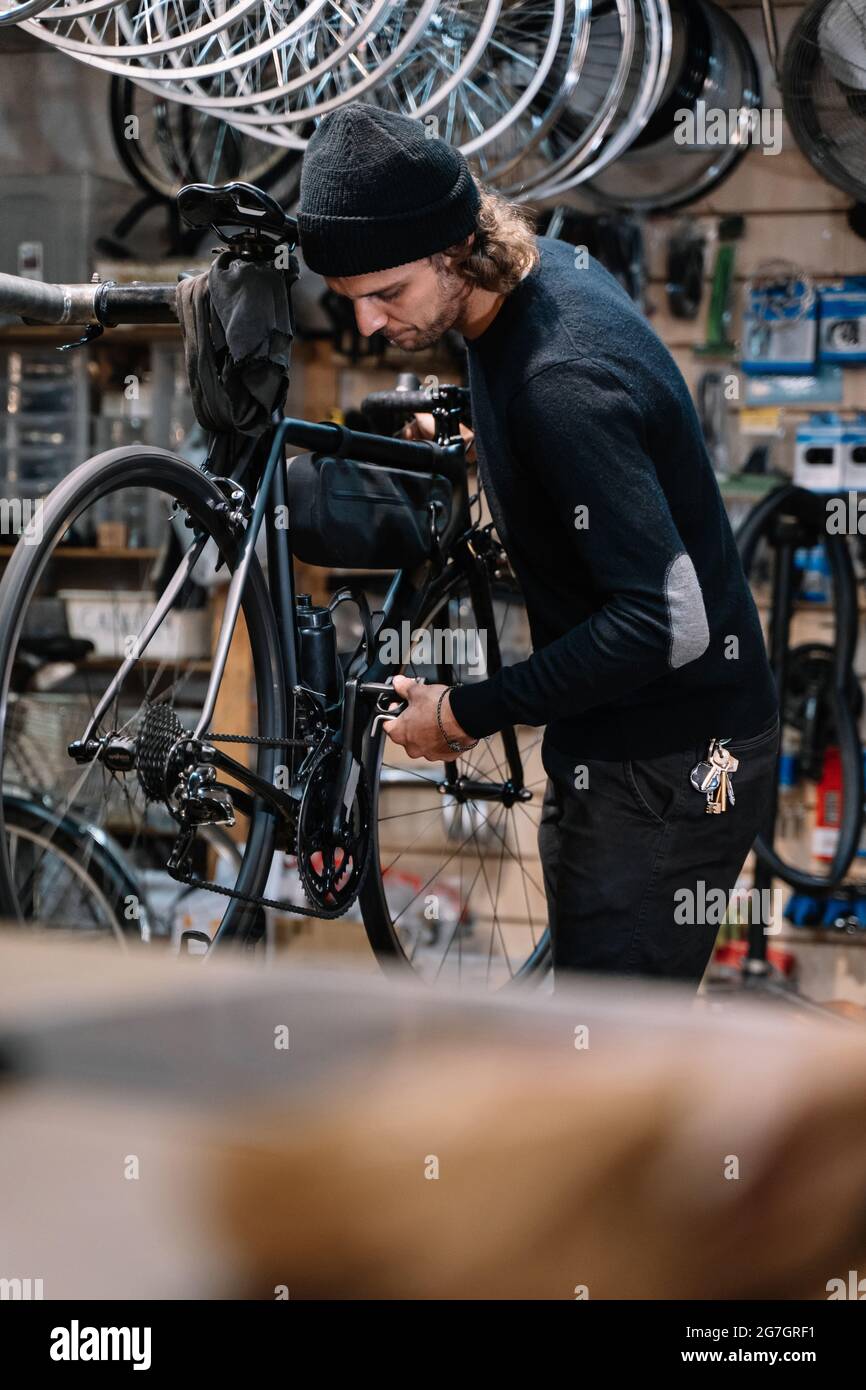 Seitenansicht des jungen erfahrenen männlichen Mechanikers mit Werkzeug Montage Kettenrad auf Fahrrad während der Reparatur Service-Arbeiten in der Werkstatt Stockfoto