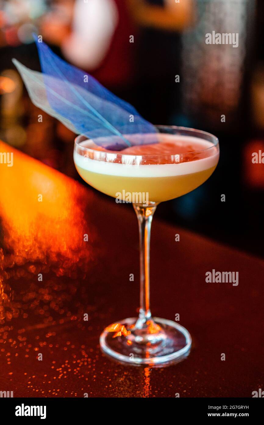 Moderner saurer Cocktail in elegantem Coupé-Glas, garniert mit kreativer blauer Dekoration, serviert an der Theke Stockfoto