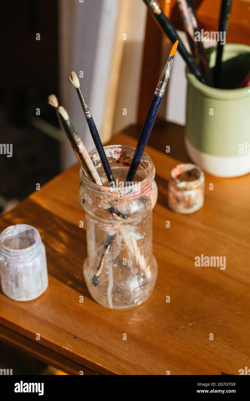 Oben verschiedener Pinsel, die im Glasgefäß auf dem Holztisch in der Kunstwerkstatt aufgestellt sind Stockfoto