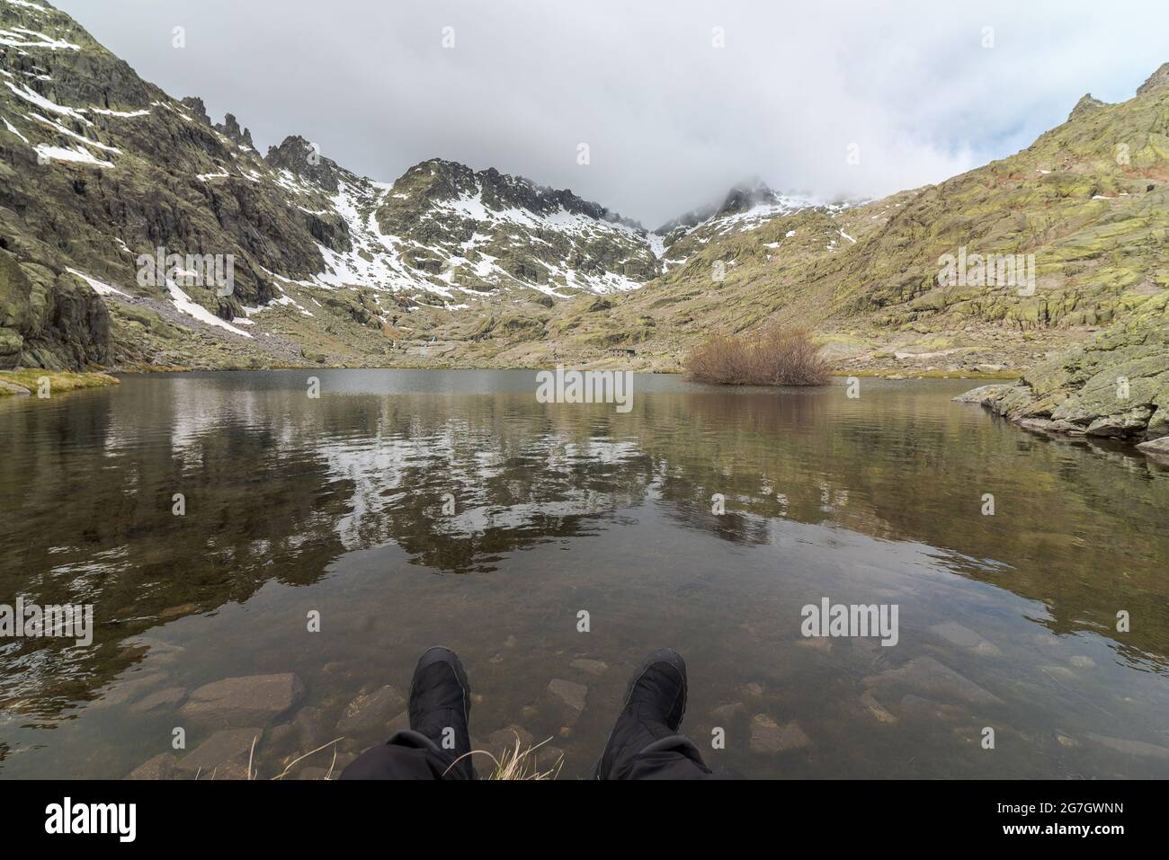 POV des anonymen Touristen, der sich an der Küste des friedlichen Sees Laguna Grande im circo de Gredos, umgeben von verschneiten Bergen in Avila, Spanien, ausruhte Stockfoto