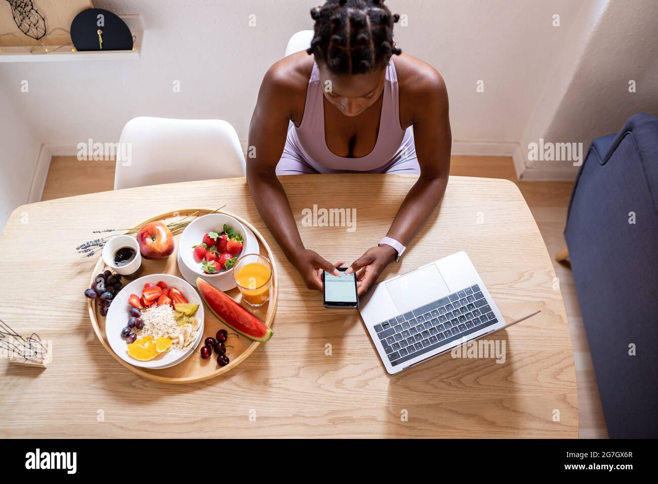 Von oben afroamerikanische weibliche Surfen Handy, während am Tisch mit reifen gesunden Früchten zu Hause sitzen Stockfoto