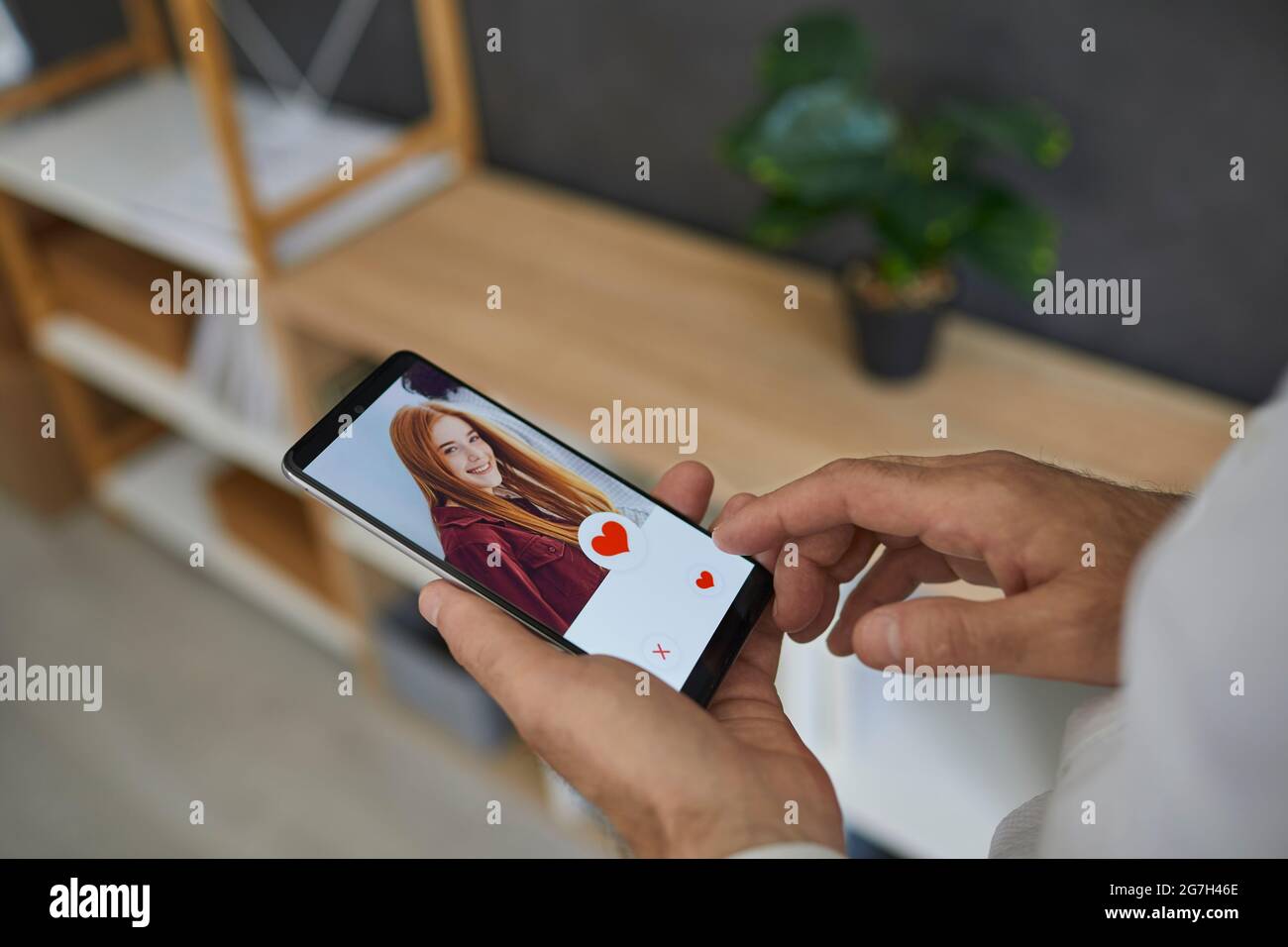 Männlicher Finger greift in der Online-Dating-App auf mobilen Smartphones nach Herztaste auf dem Bildschirm. Stockfoto