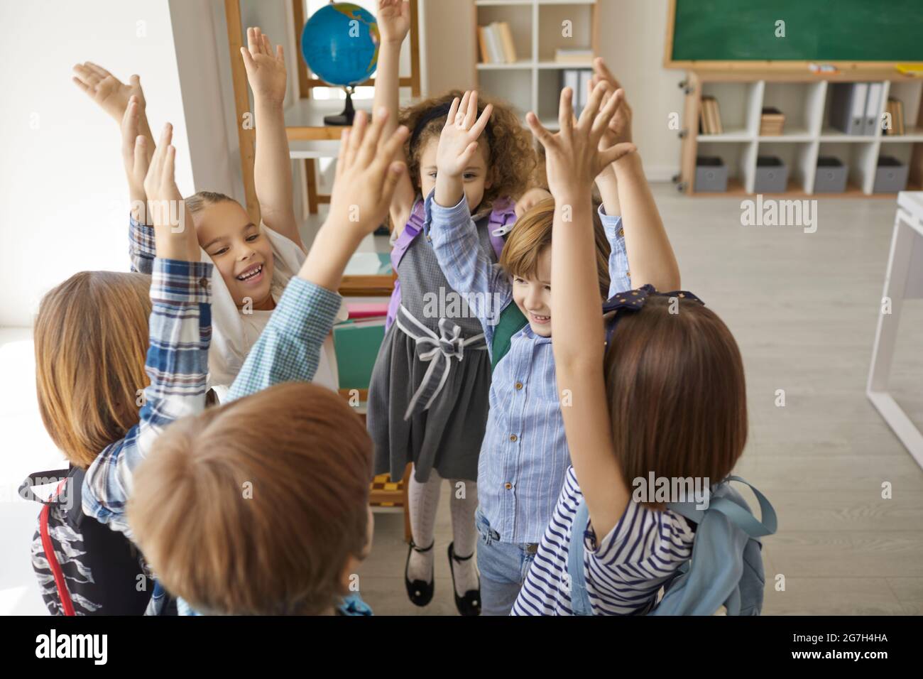 Eine Gruppe von fröhlichen, aufgeregten kleinen Schulkindern legte die Hände hoch und schrie Hurray Stockfoto