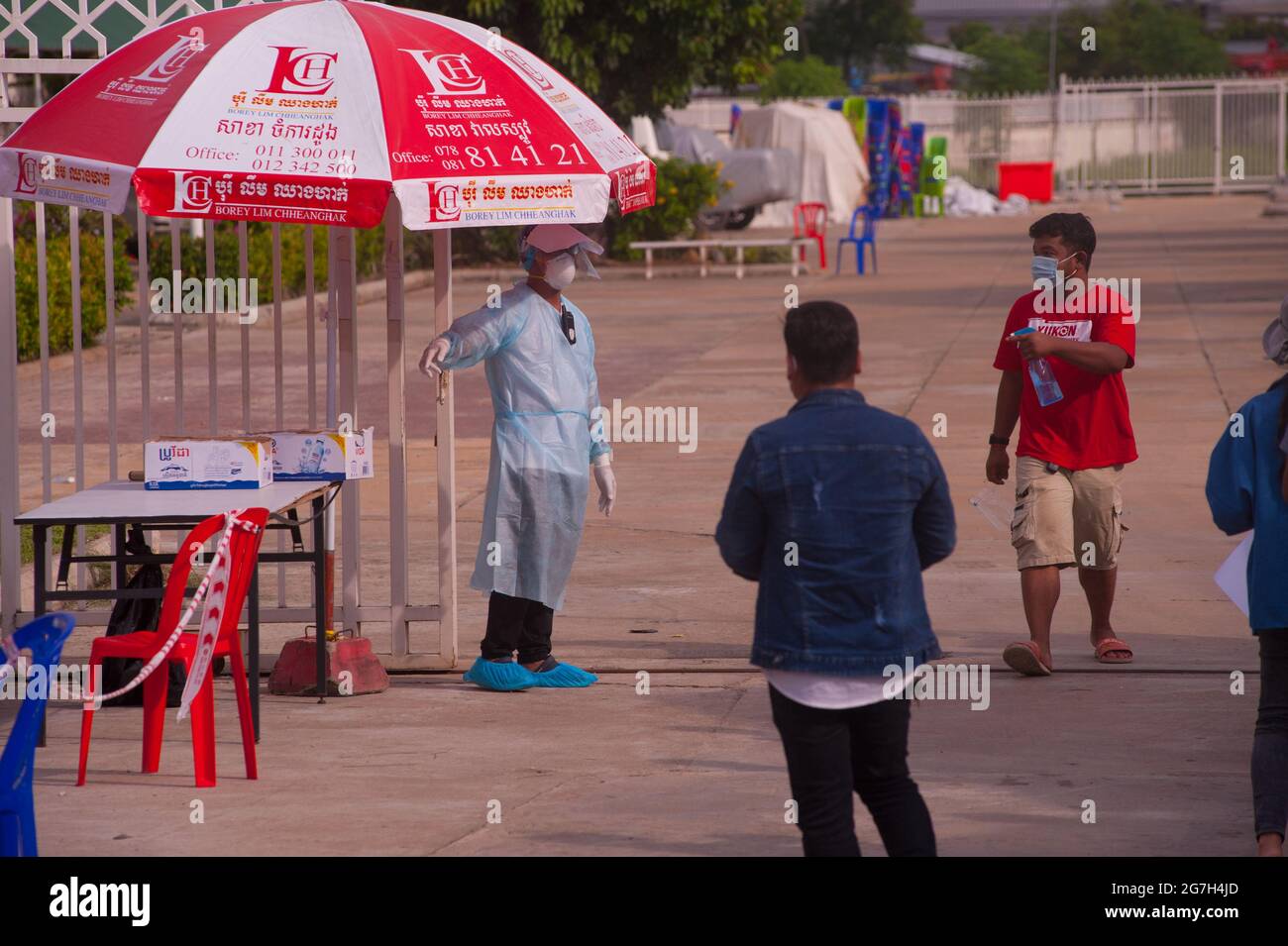 Phnom Penh, Kambodscha. 14. Juli 2021. Seit fast 5 Monaten kämpft Phnom Penh gegen einen COVID - 19-Anstieg. Ein EMT/Sanitäter in voller PSA leitet eine Massenteststelle, während ein kambodschanischer Mann mit einer Flasche Händedesinfektionsmittel/Desinfektionsmittel auskommt. Quelle: Kraig lieb / Alamy Live News Stockfoto